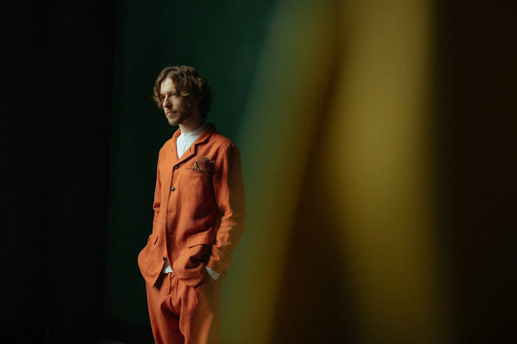 About: a man in a bright orange suit stands under coloured stage light, photographed by Andrei Kovalev.