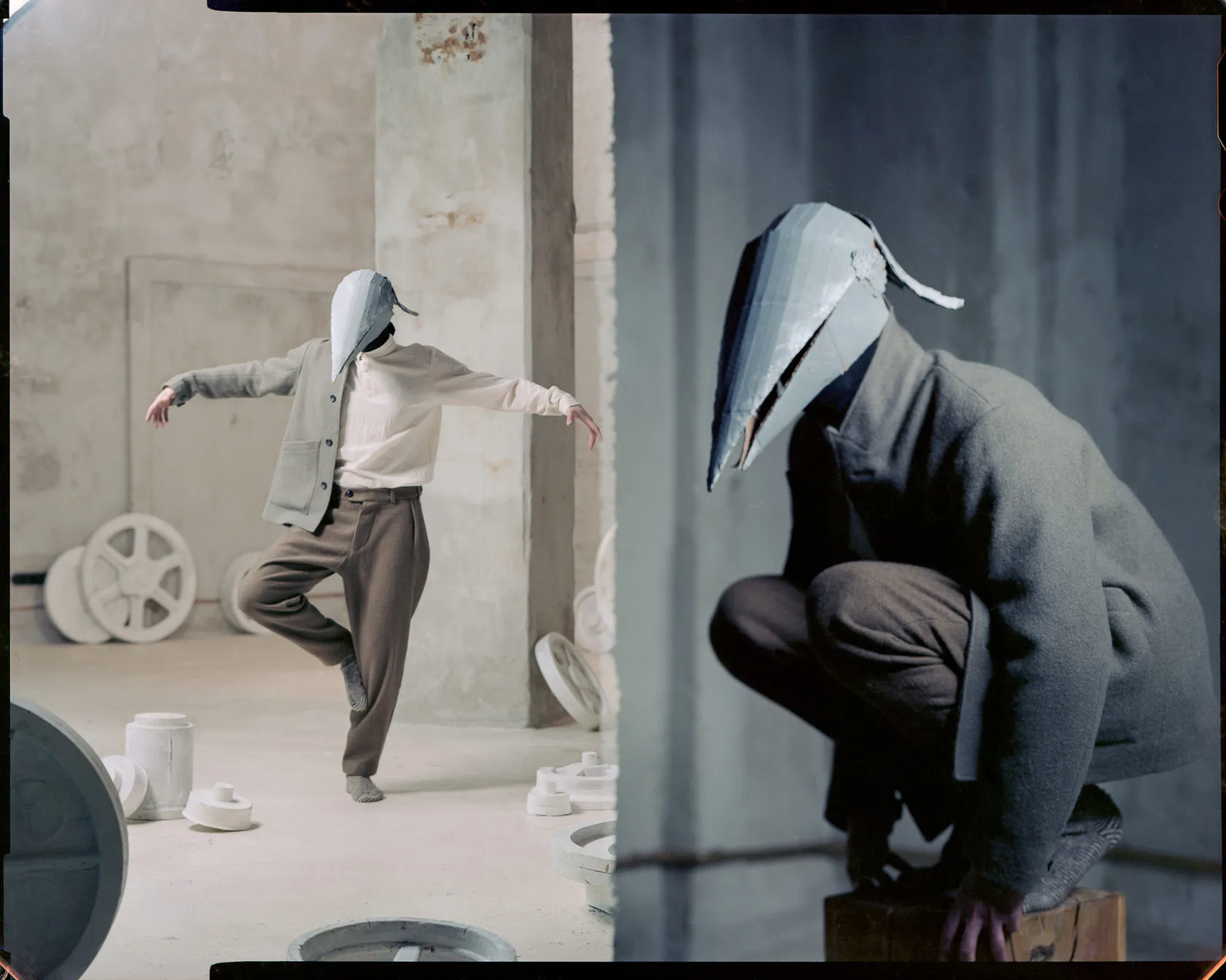 A man in a pointed cardboard mask balances on one leg among white wheels, and crouches on a box in close-up.