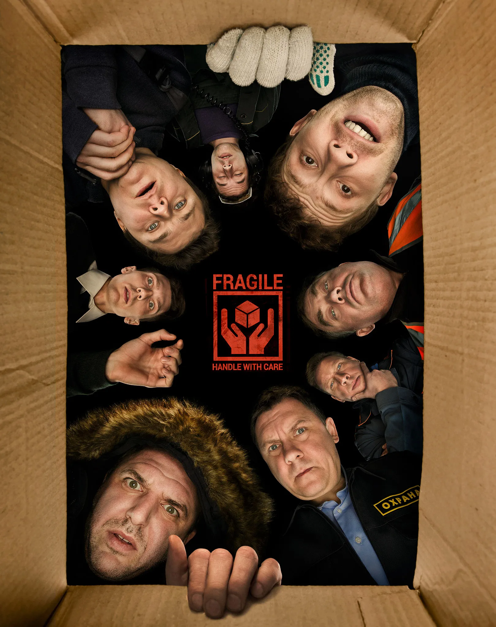 The cast’s faces crammed into a cardboard box marked Fragile, looking up.