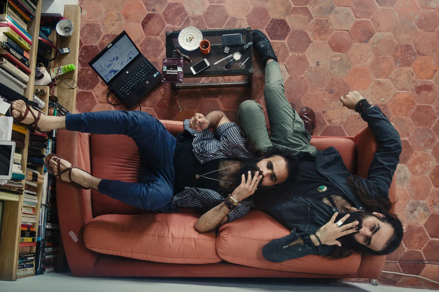 Tarzan and Arab Nasser sprawl on a red sofa, shot from above beside a bookcase.