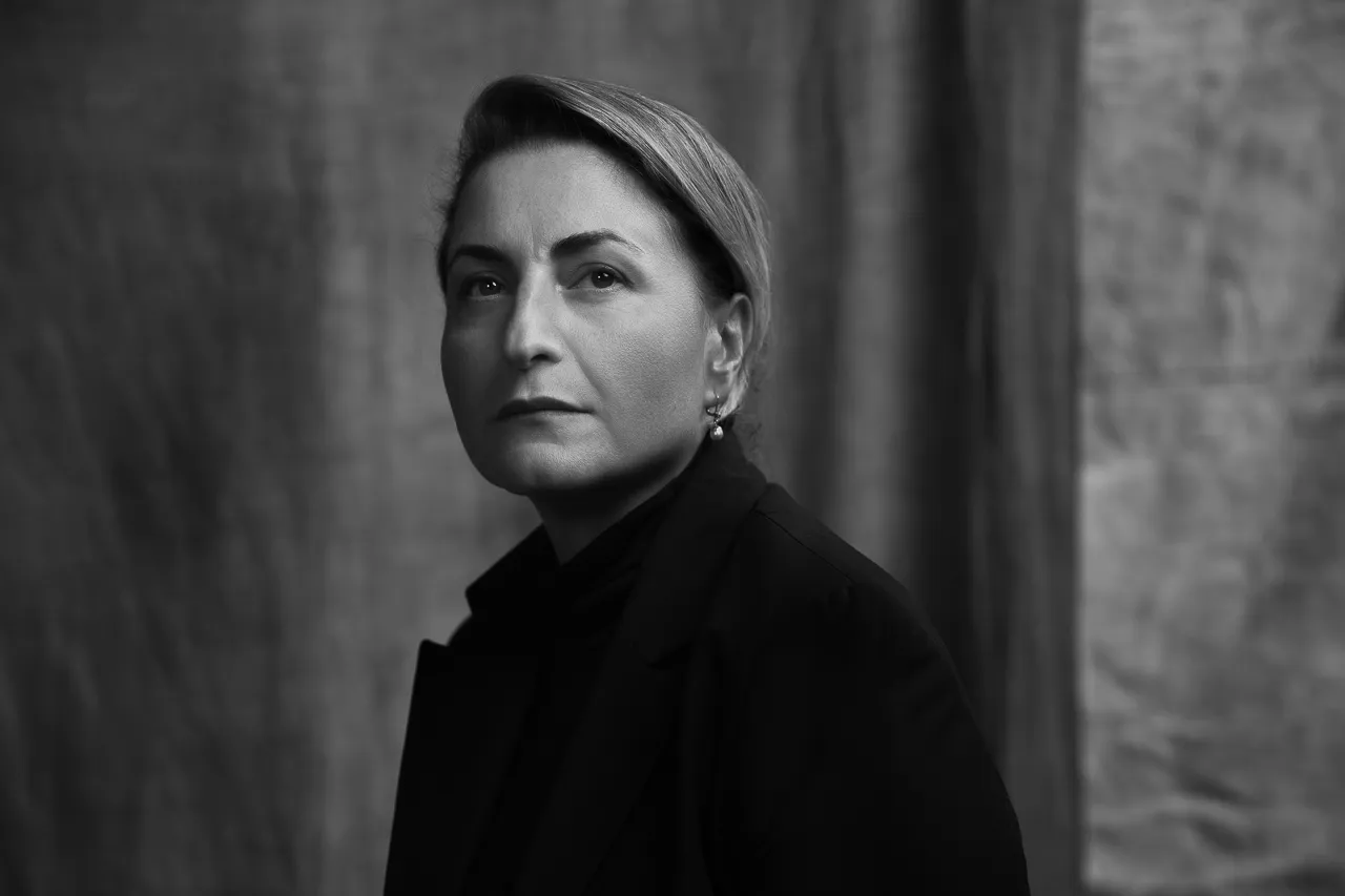 Sofia Khorguani in a black coat against a grey backdrop, in black and white.