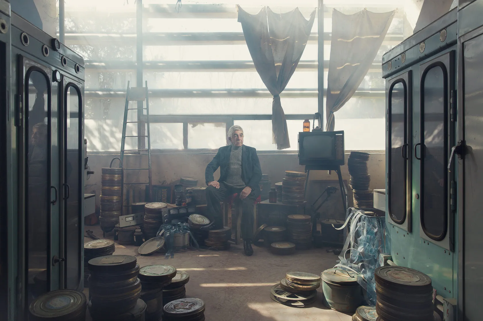 Robert Durakyan sits on a stool among film cans in a sunlit studio hall.