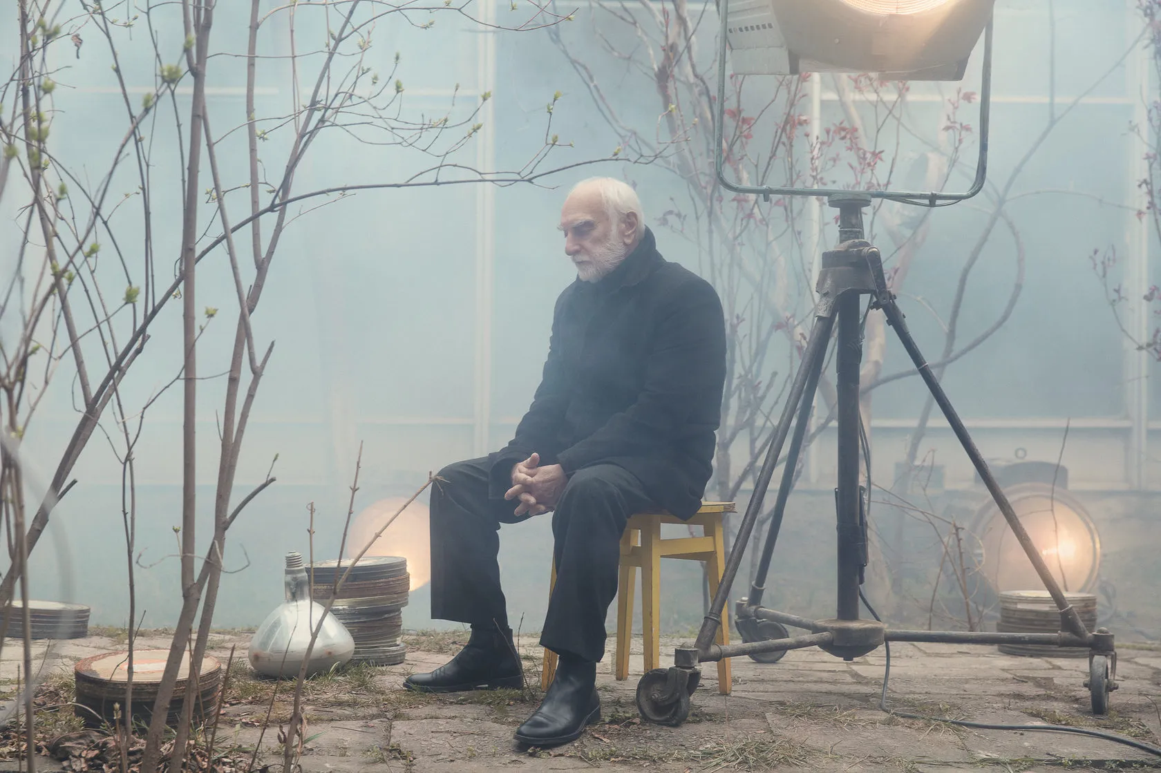Batoni Merab sits on a yellow chair under a spotlight in the misty courtyard.