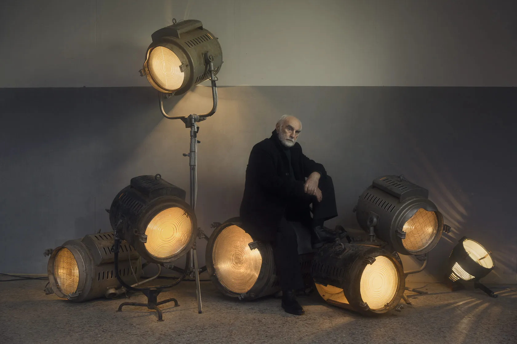 Batoni Merab sits among old studio spotlights against a grey wall.