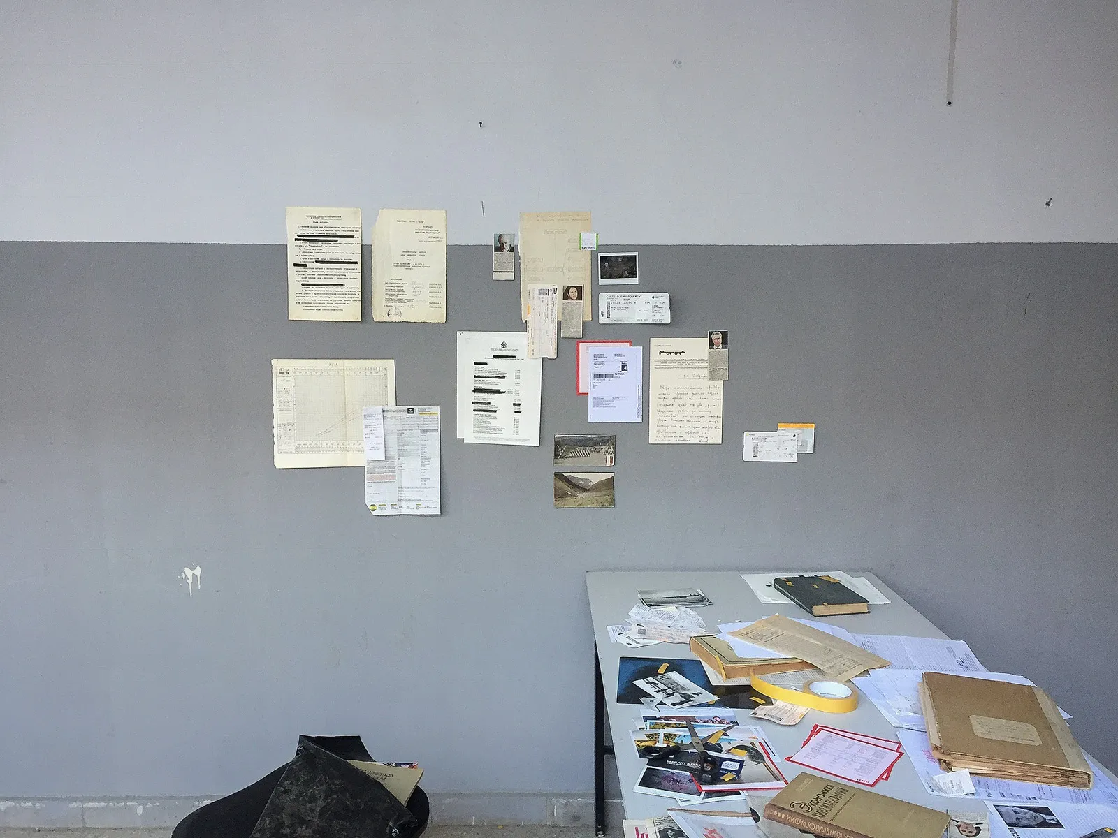 Papers pinned to a grey wall above a desk heaped with files.