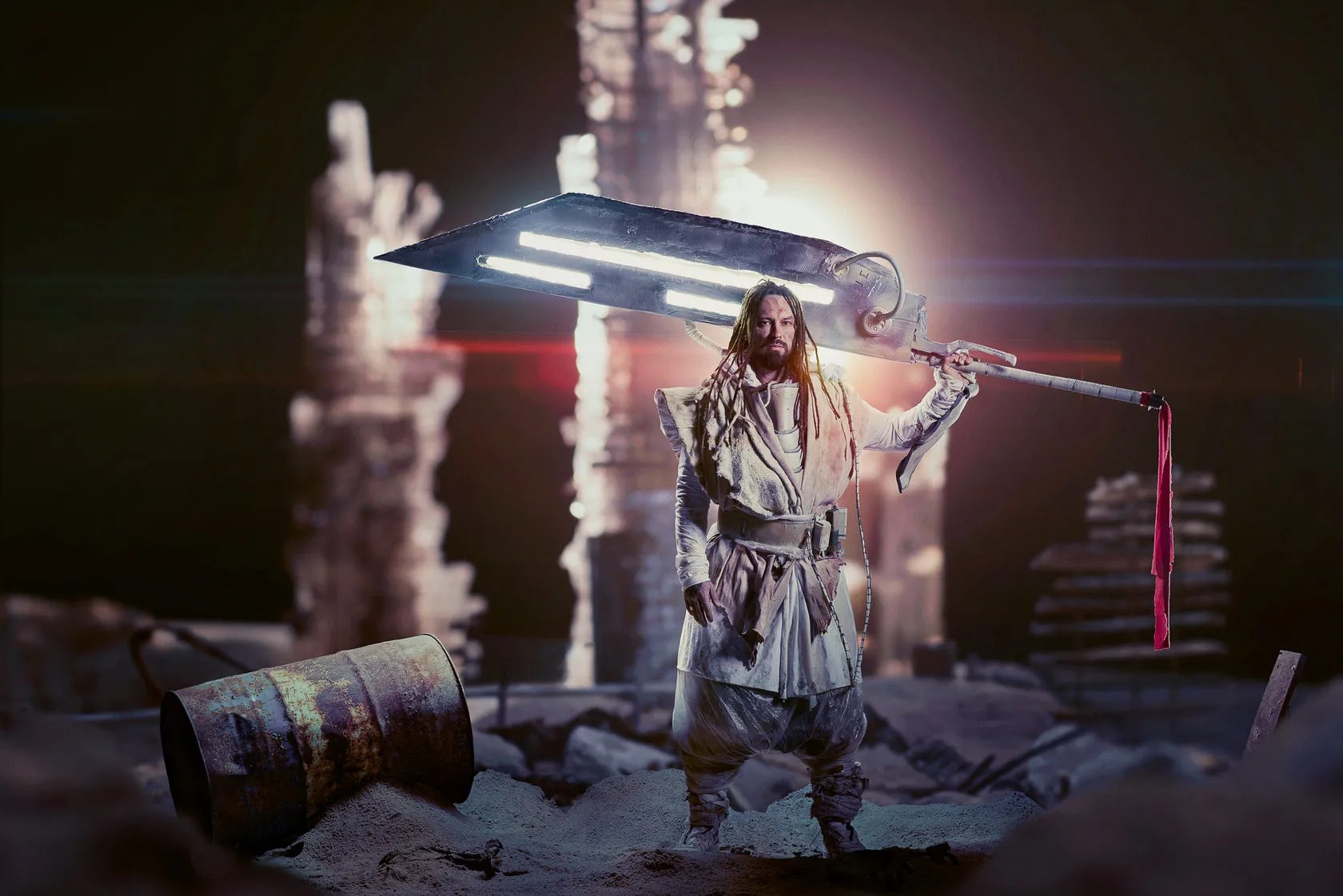 The samurai raises a huge glowing blade among ruined towers, a rusty barrel at his feet.