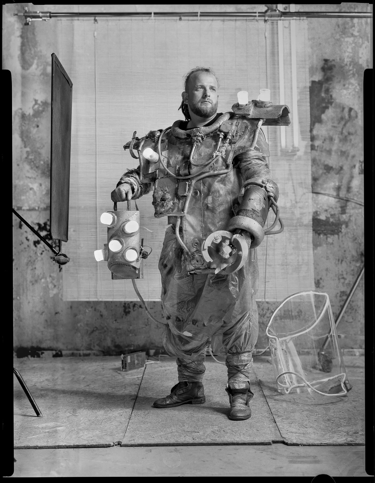 The Deepwater Treasure Hunter in a battered diving suit hung with lamps, on black-and-white sheet film.