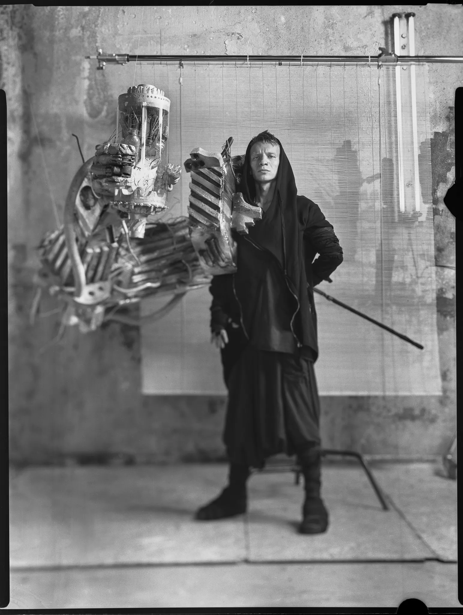 The Robo-Tomb Raider in a black hood, a huge mechanical arm on his shoulder, on black-and-white sheet film.