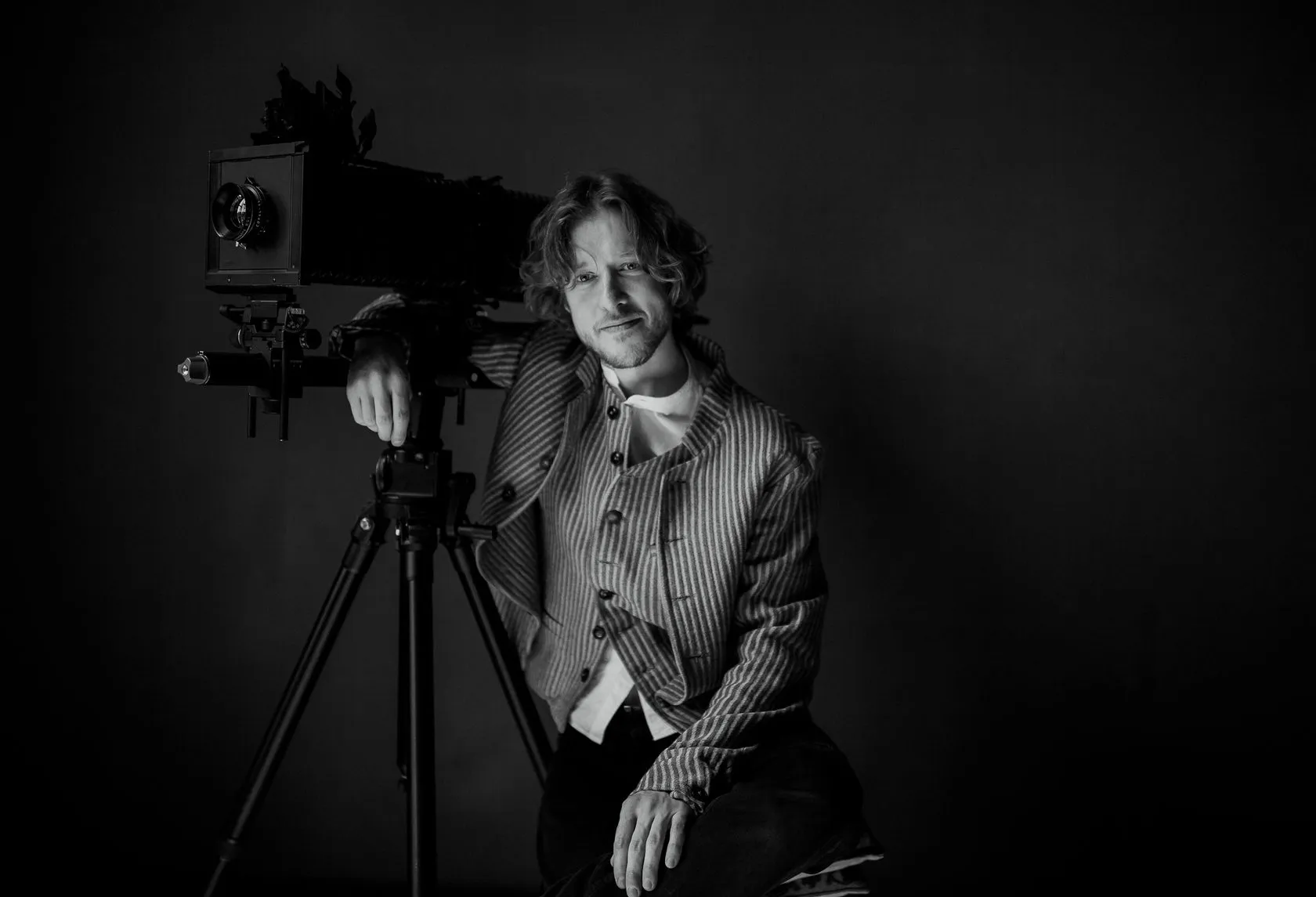 Consulting by Andrei Kovalev: a man poses beside a large-format view camera in a striped vintage vest.