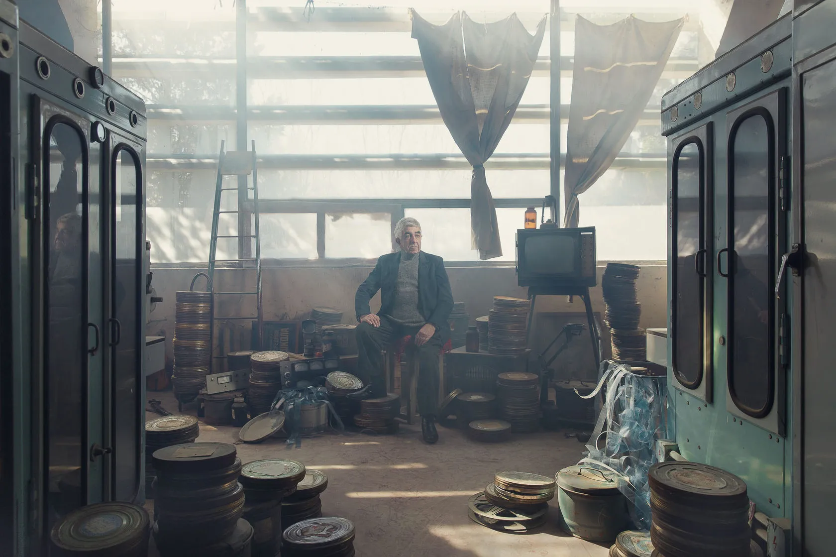 Robert sits among stacks of film cans in a sunlit studio hall, an old television beside him.
