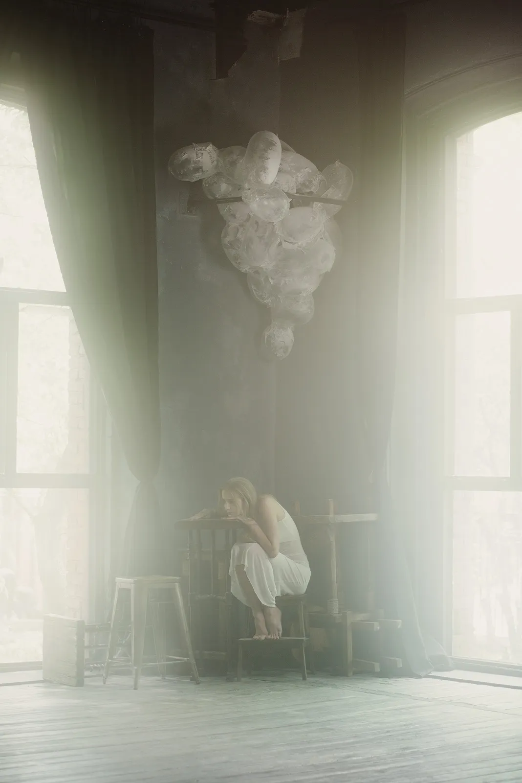 A woman crouches on a stool in a misty hall flooded with window light, the cloud hanging above.