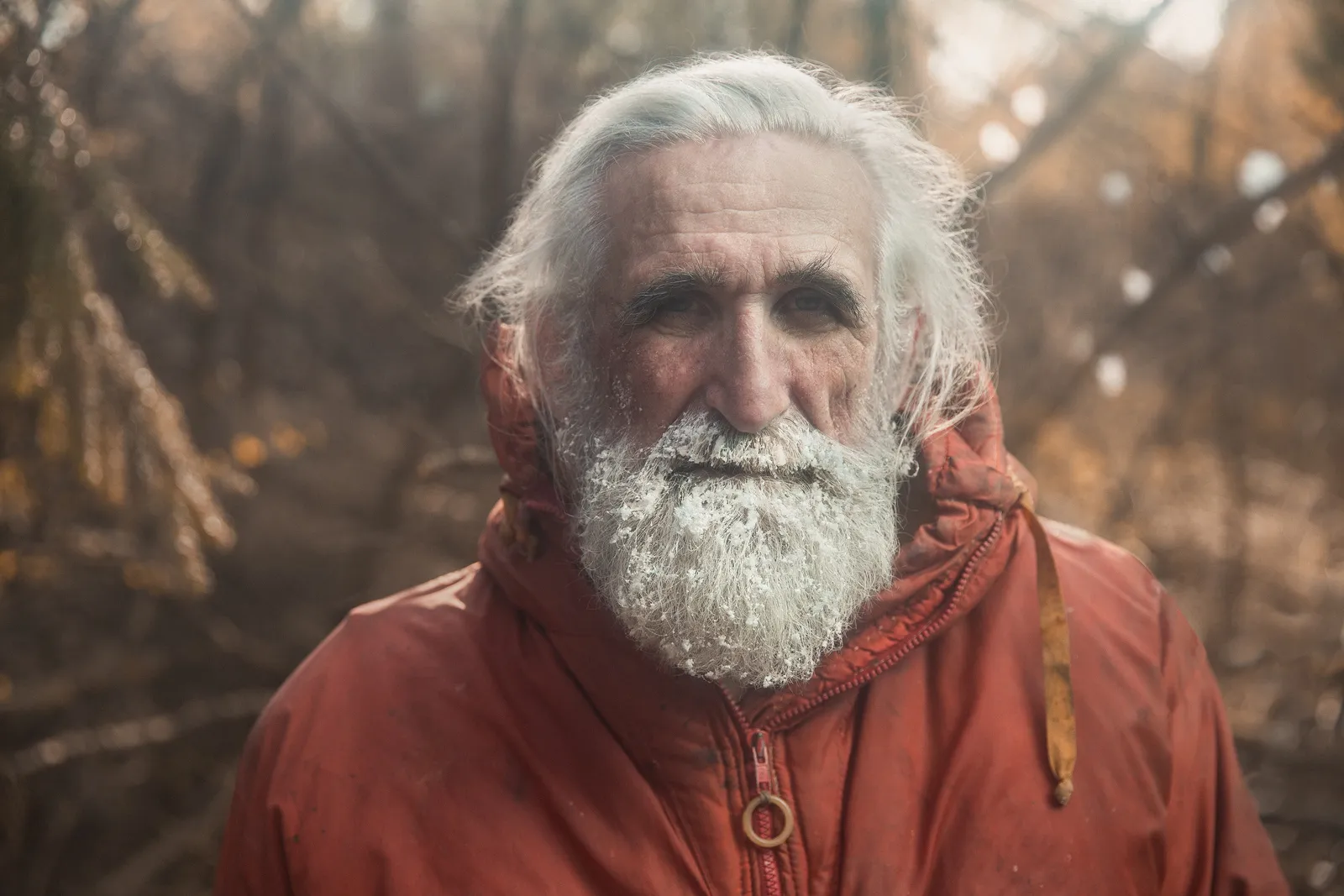 Vladimir Chukov, white-bearded, in a red parka among autumn trees.