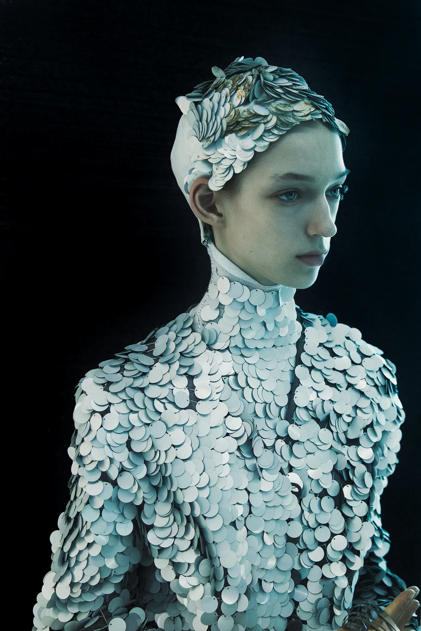 A model in a costume of silver scales against a black background.