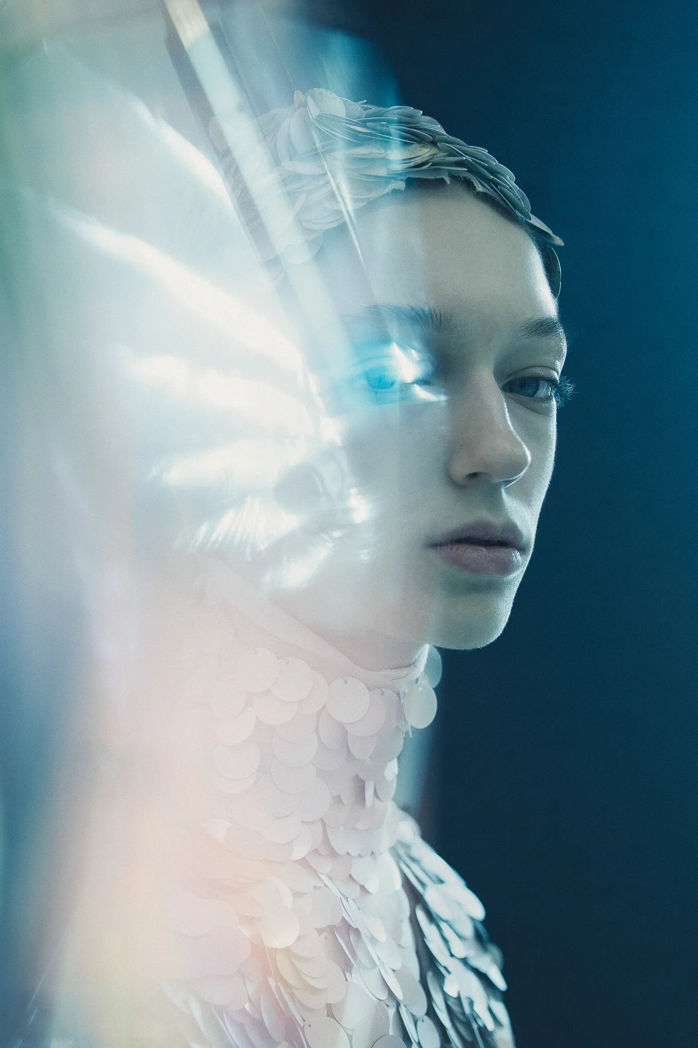 The model in silver scales in close-up, light flaring across her face.