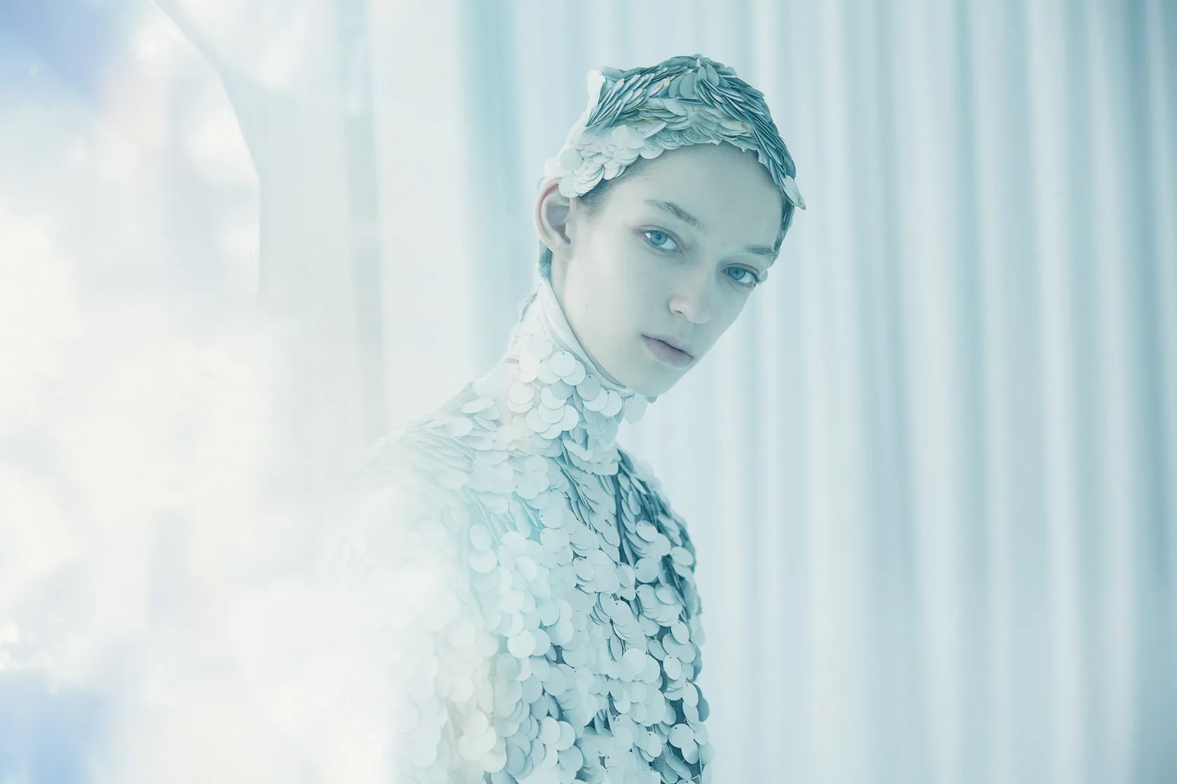 The model in a scaled headpiece looks over her shoulder in pale blue light.