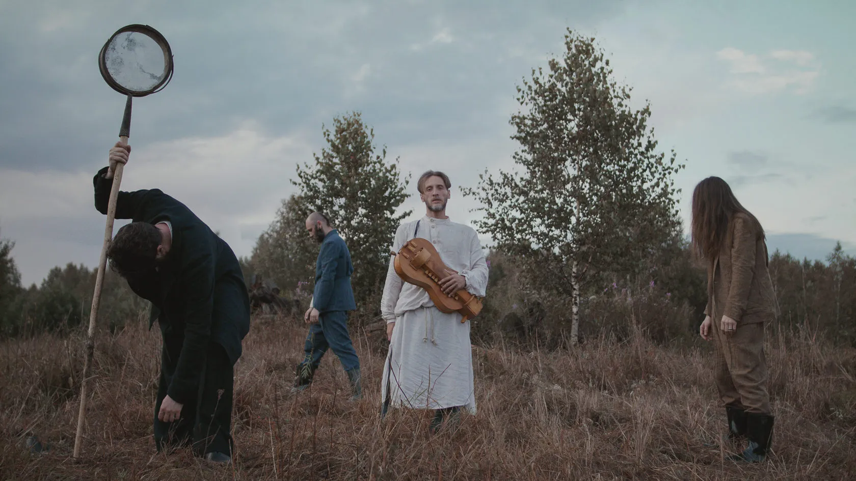 Four figures in a heath field: one stoops with a long staff, one in white holds a hurdy-gurdy.