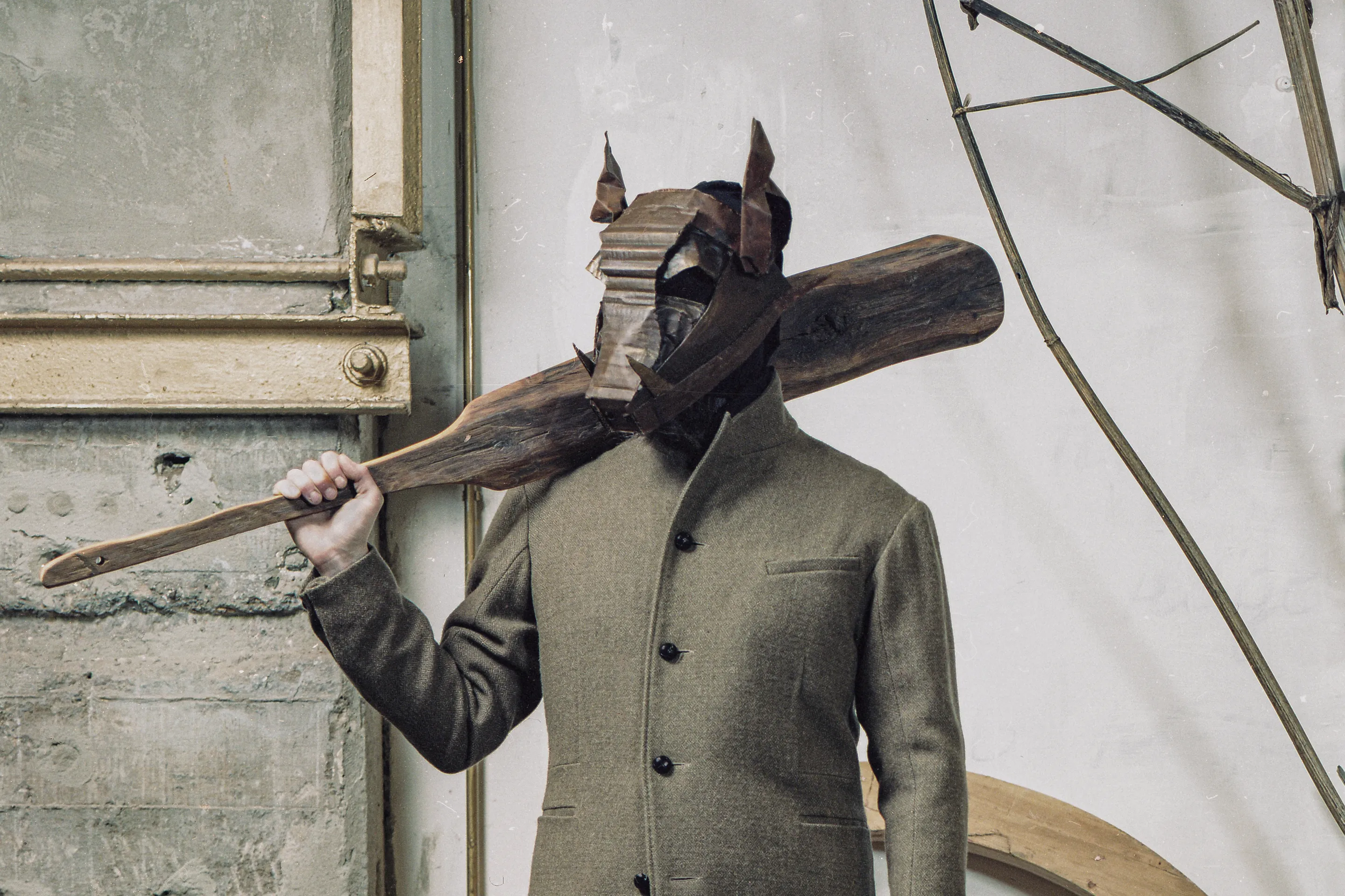 Infundibulum Fair by Andrei Kovalev: a model in a horned patchwork mask carries a wooden plank over one shoulder.