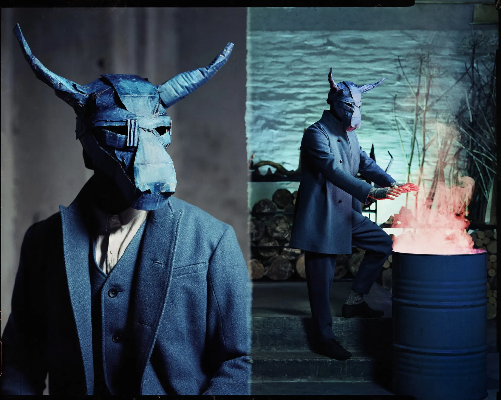 A blue horned mask in close-up, and its wearer warming his hands over a burning barrel.