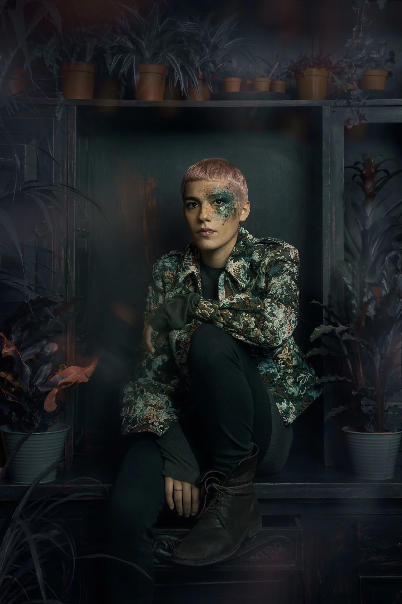 The model sits in the niche in the floral jacket, green glitter across one eye.