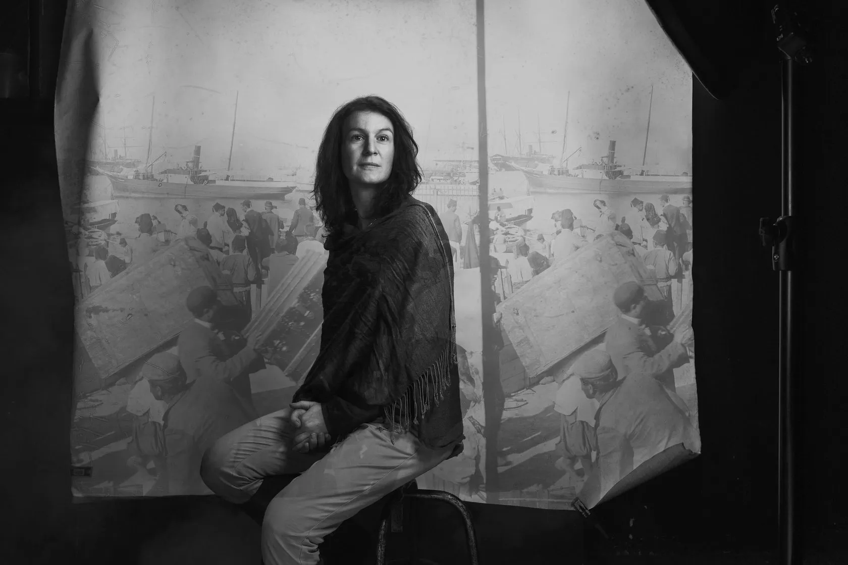 Olga Lossky sits in front of a printed seaside backdrop, in black and white.