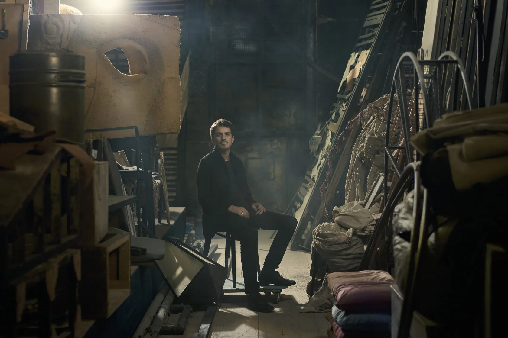 Sven Hansen-Løve sits among old stage props and scenery in a theatre store.