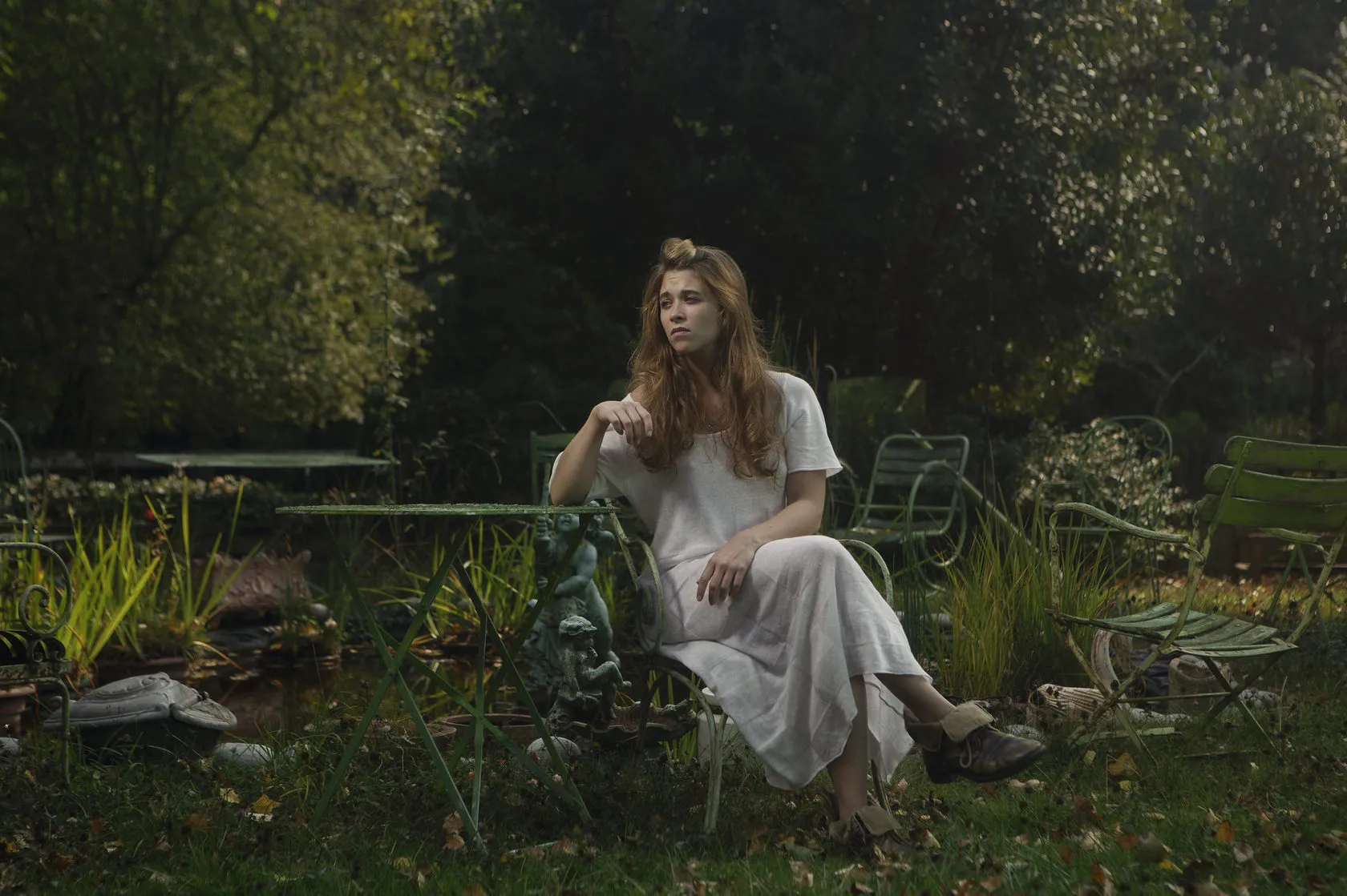 Emma sits in a white dress among green garden chairs and plants.