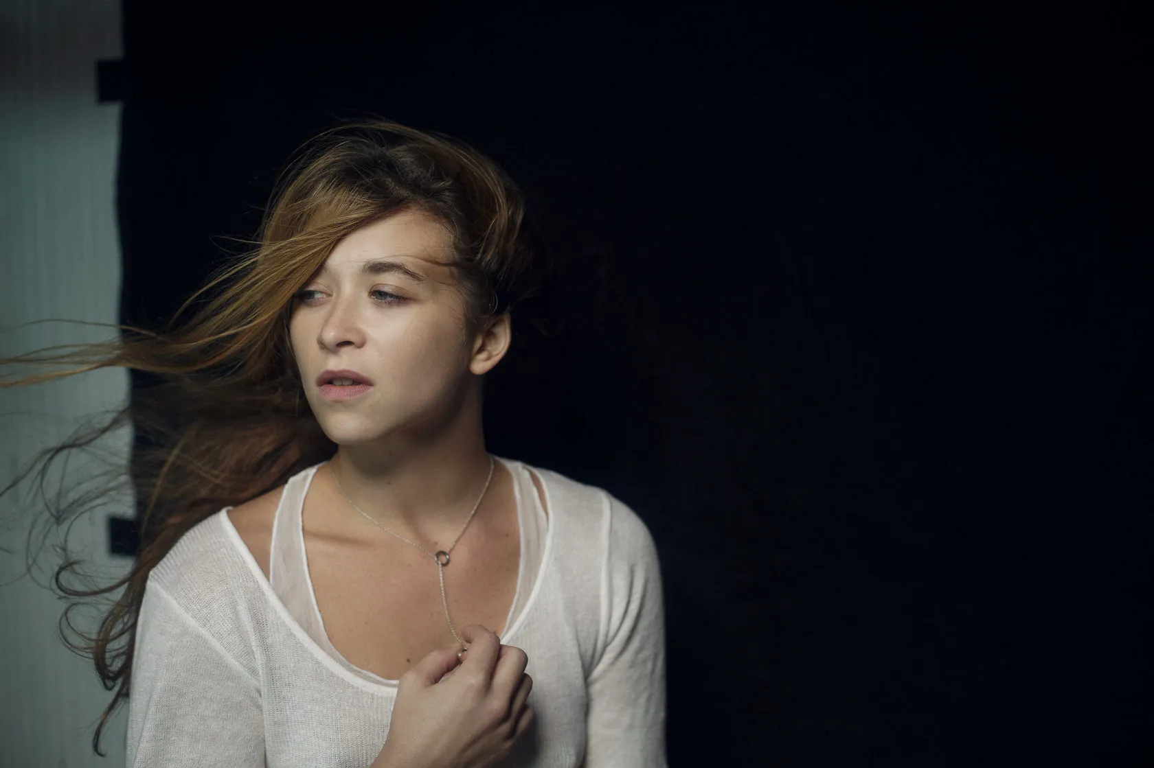 Emma looks away in the dark, hair blowing, a hand at her chest.