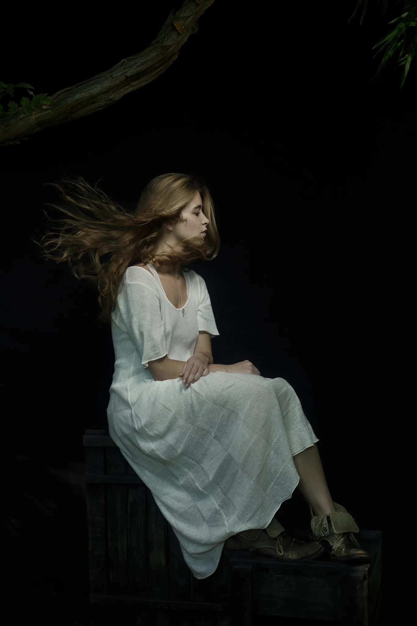 Emma sits on a crate in a white dress at night, her hair blowing.