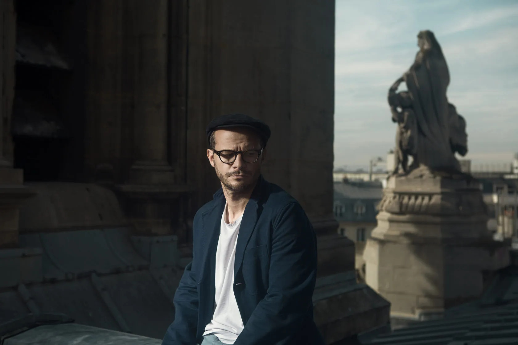 Laurent in a flat cap on the roof, a statue and the Paris skyline behind him.