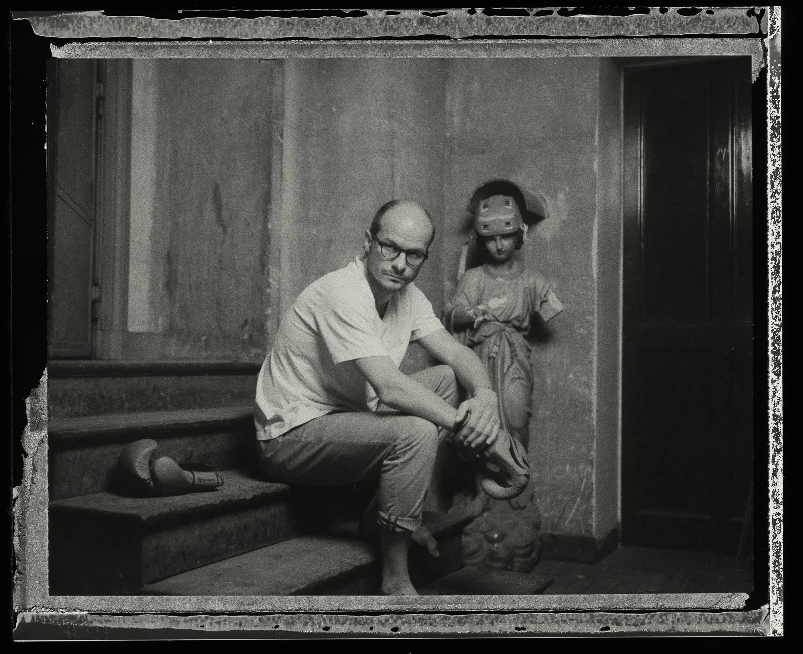 Laurent sits on the steps in a white T-shirt beside a statue, on old instant film.
