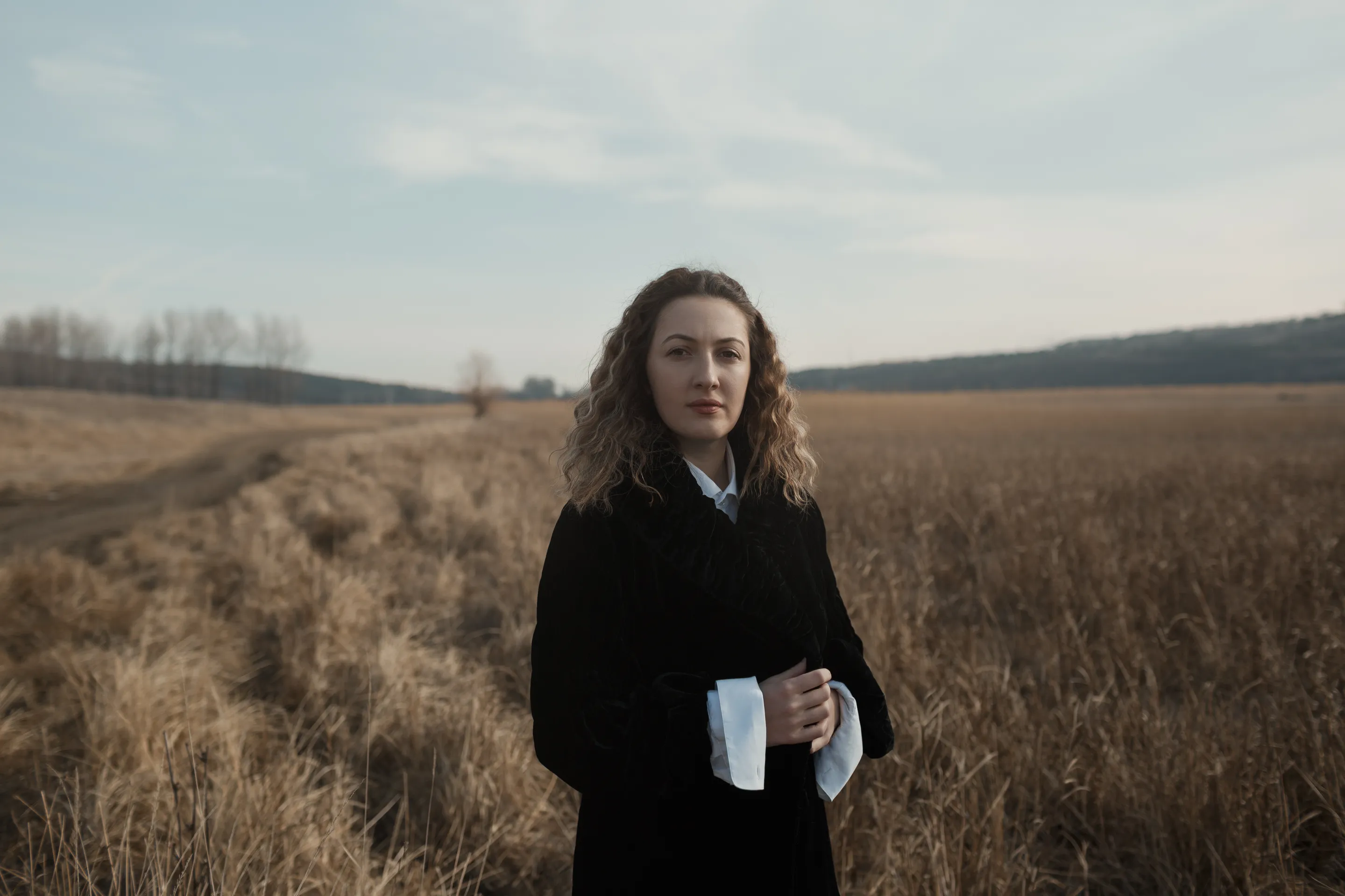 Marika by Andrei Kovalev: a woman stands alone in a golden wheat field, holding white papers.