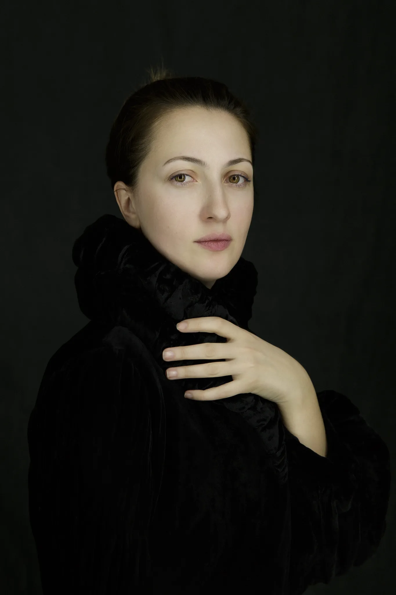 Marika holds her fur collar with one hand and looks into the camera.