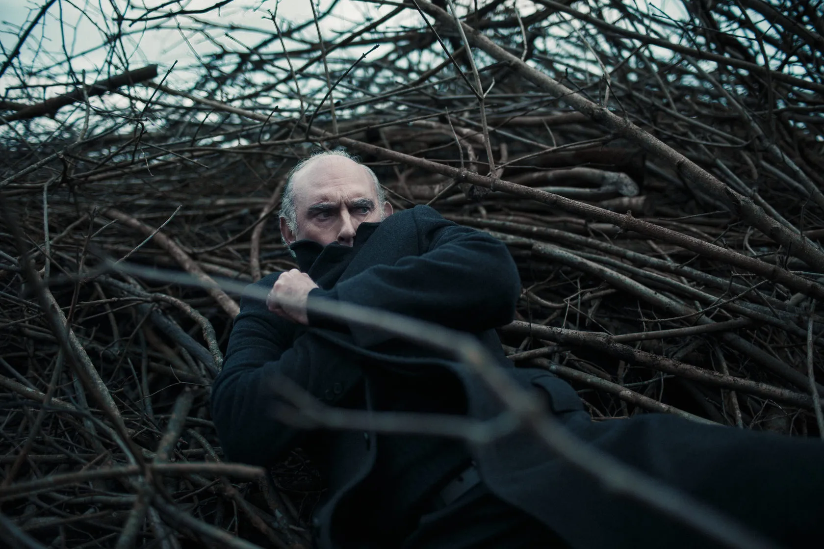 Michel lies in a heap of cut branches, holding his collar to his face.