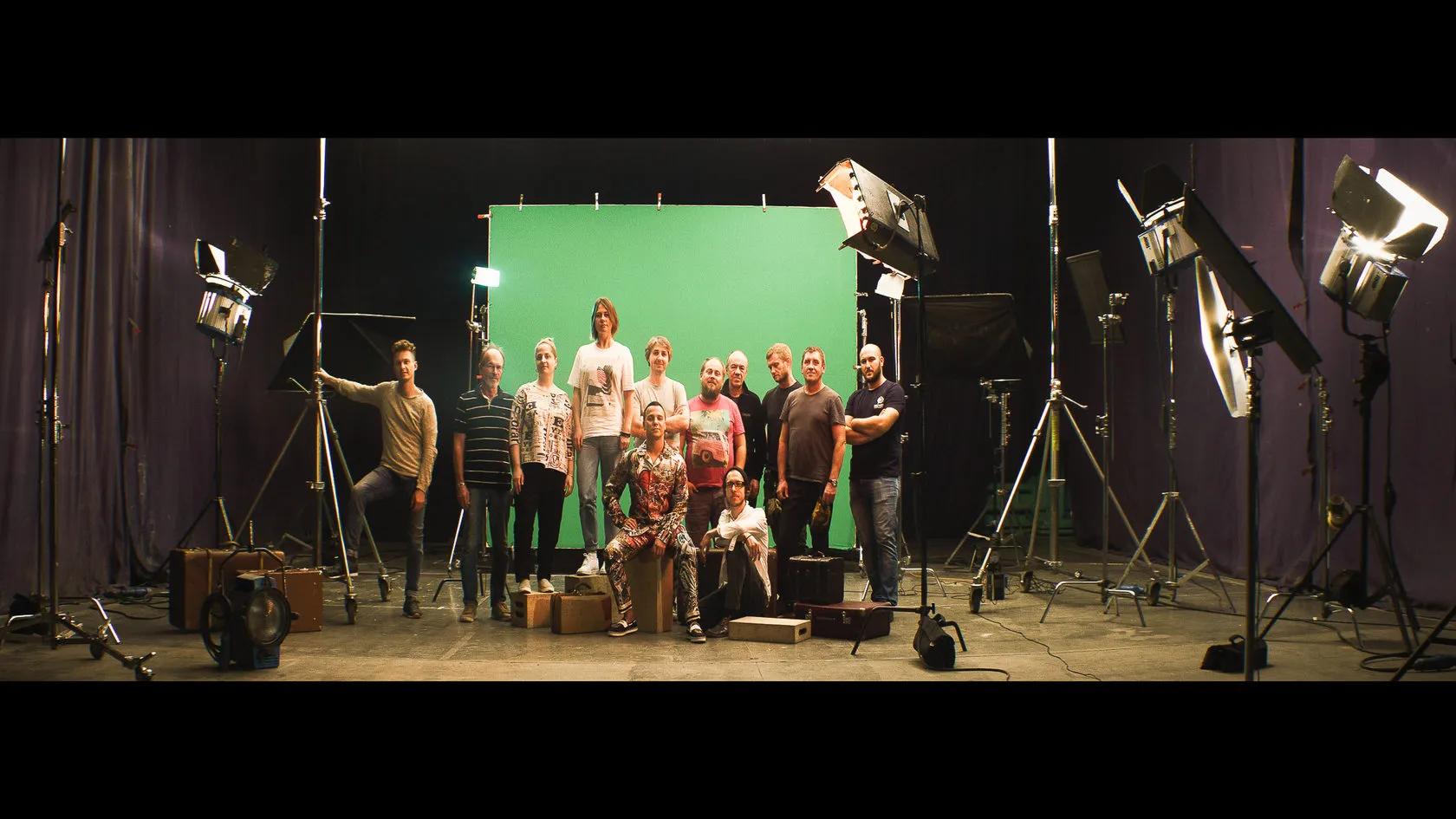 The crew poses in a studio in front of a green screen, lights all around.