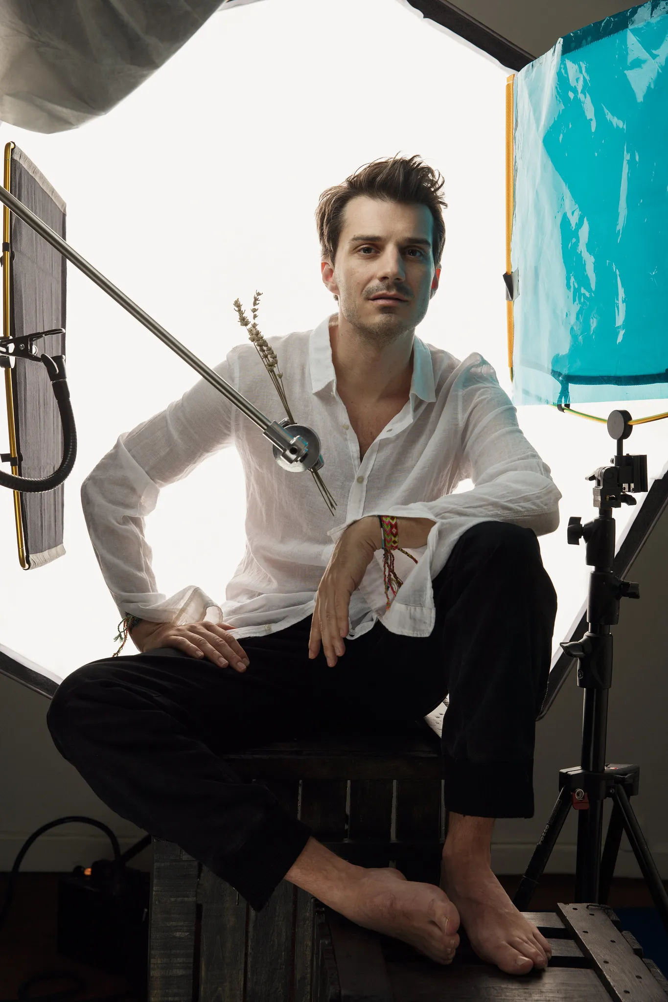 Sven Hansen-Løve sits barefoot on a wooden crate between studio lights, in a white shirt.