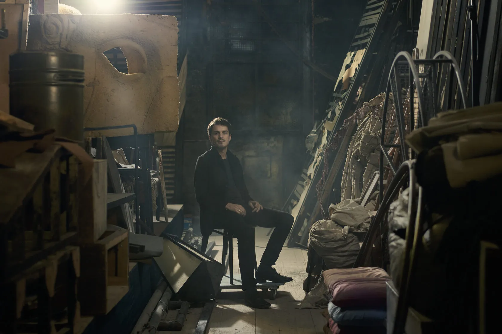 Sven sits among old stage props and scenery in a theatre store.