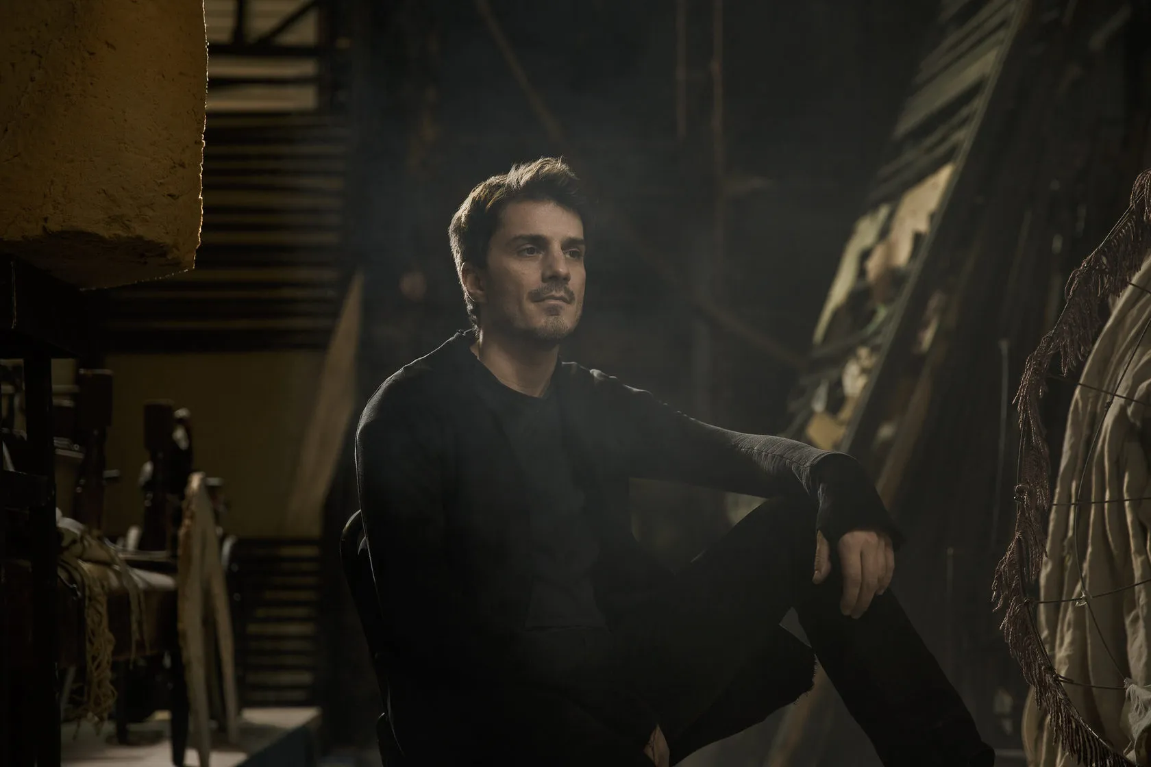 Sven sits in a dim theatre store among scenery and props.
