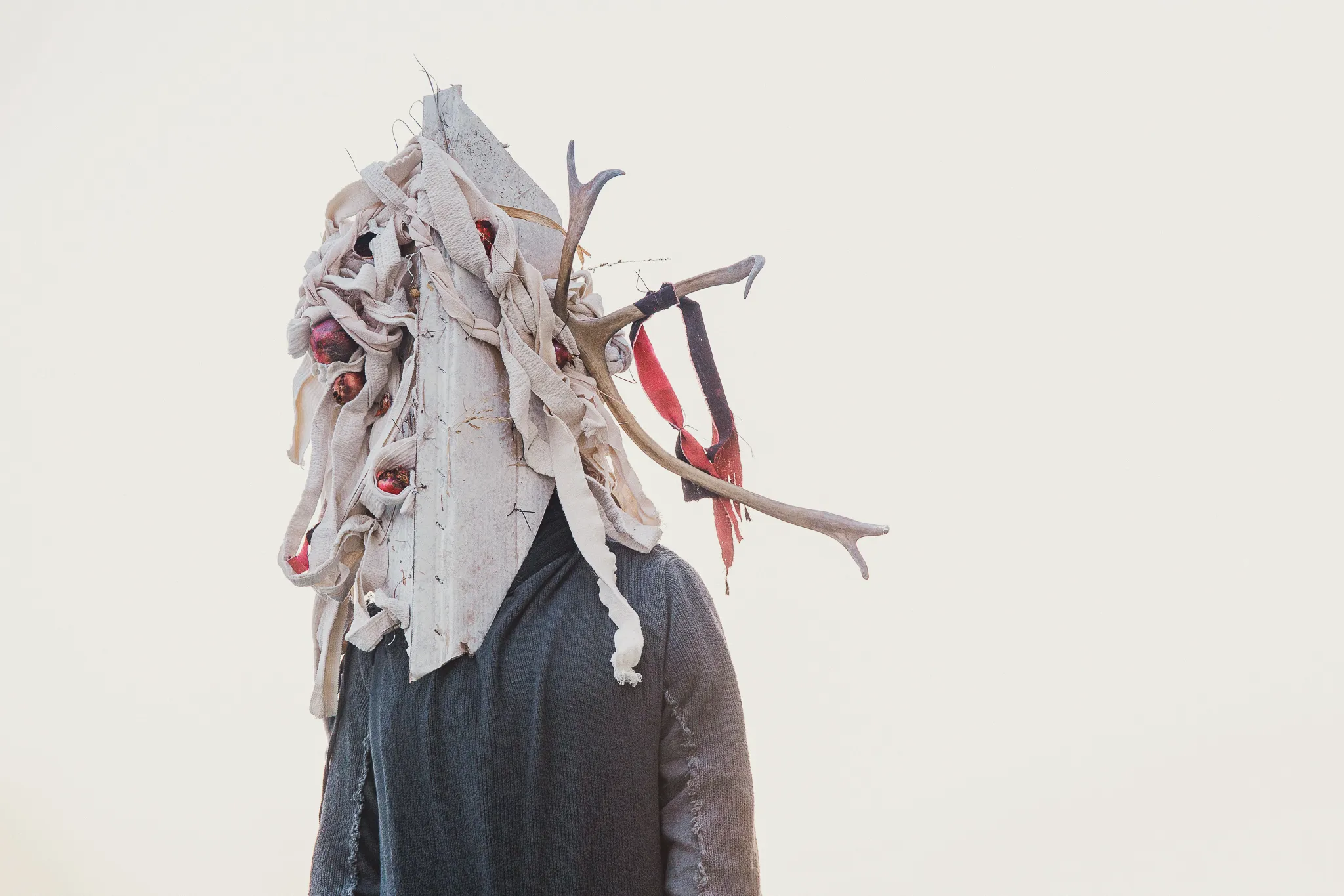 Masks portfolio by Andrei Kovalev: a model wears an antlered bone-and-branch mask against a plain pale sky.