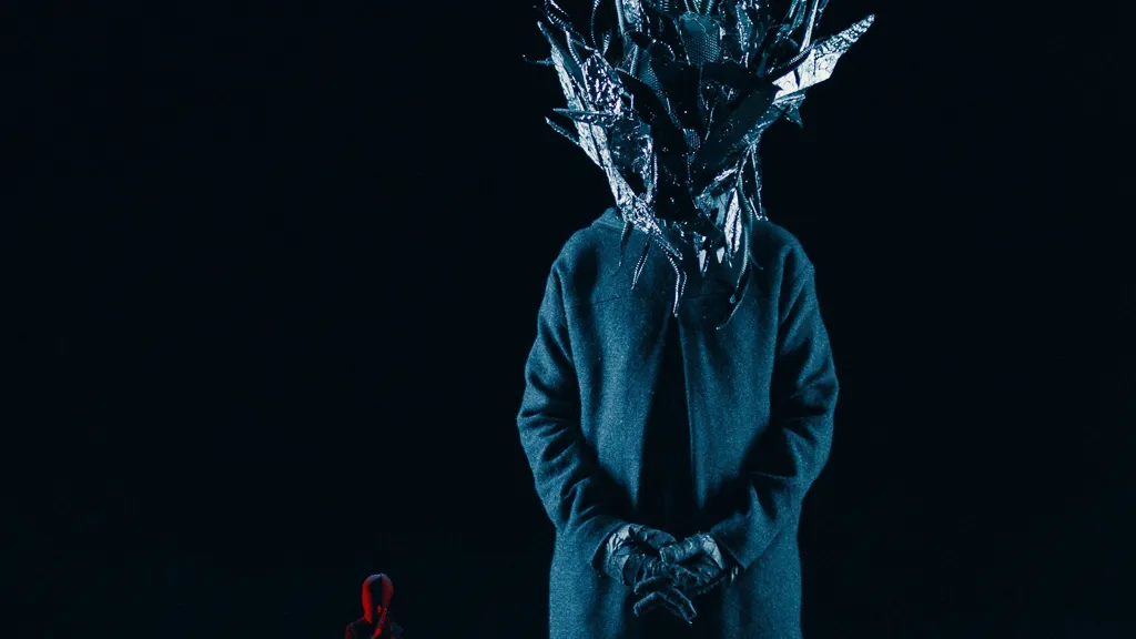 Oleg Paschenko as Chaos, in a spiky foil mask and a long blue coat, hands clasped.