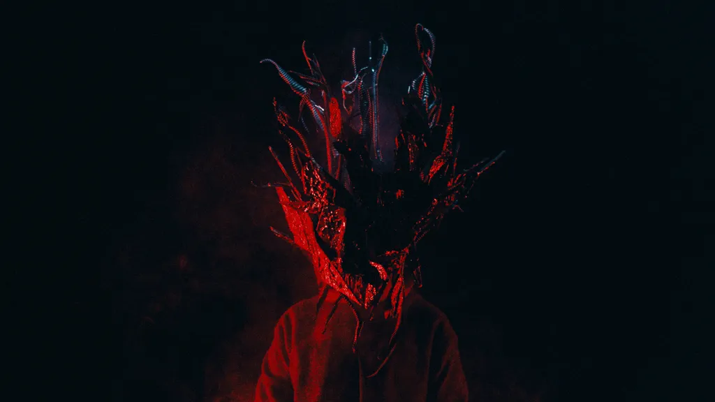 The mask lit red, the face beneath it in shadow.