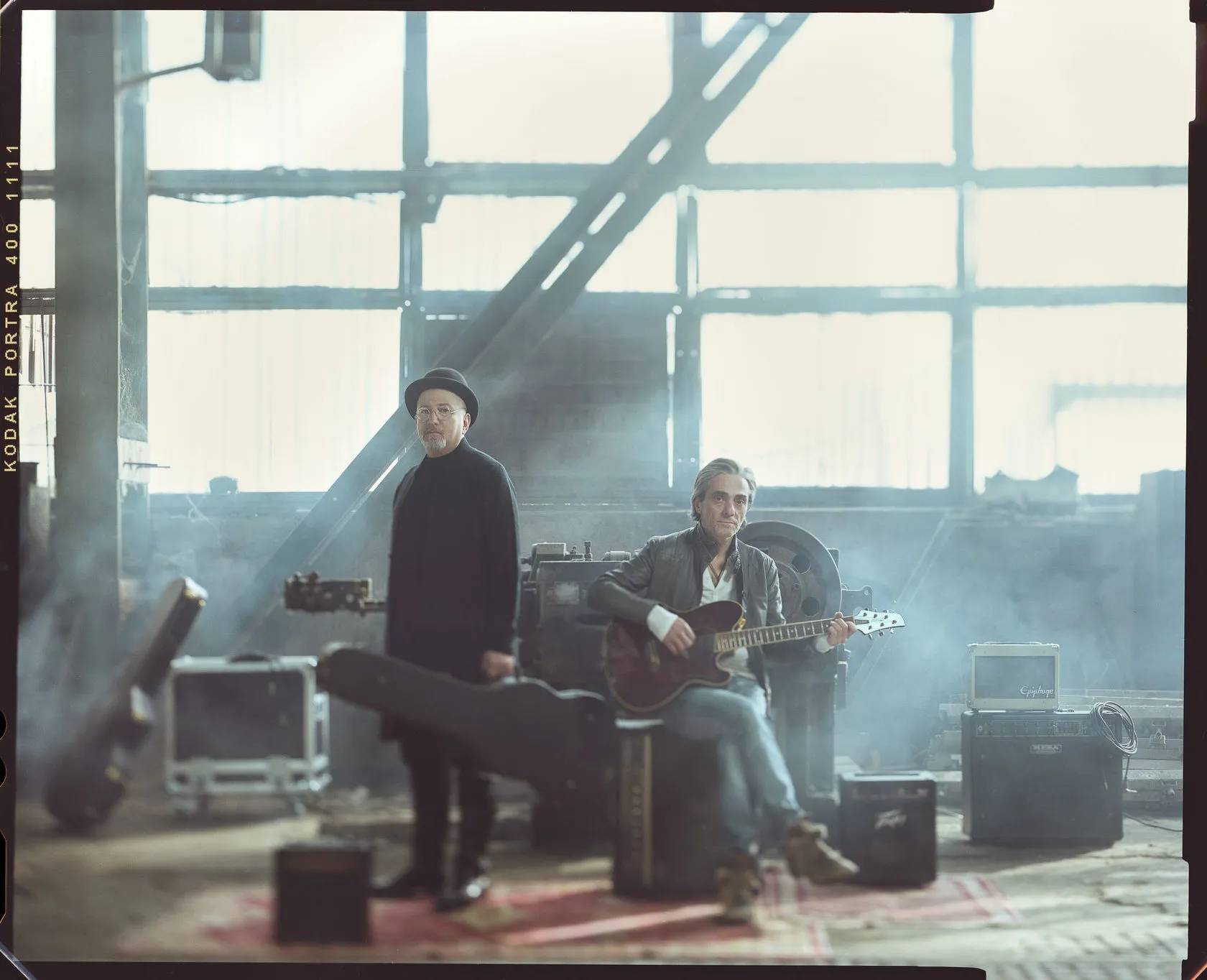 Gocha Kacheishvili and Malkhaz Abuladze with a guitar and amplifiers in a hazy factory hall.