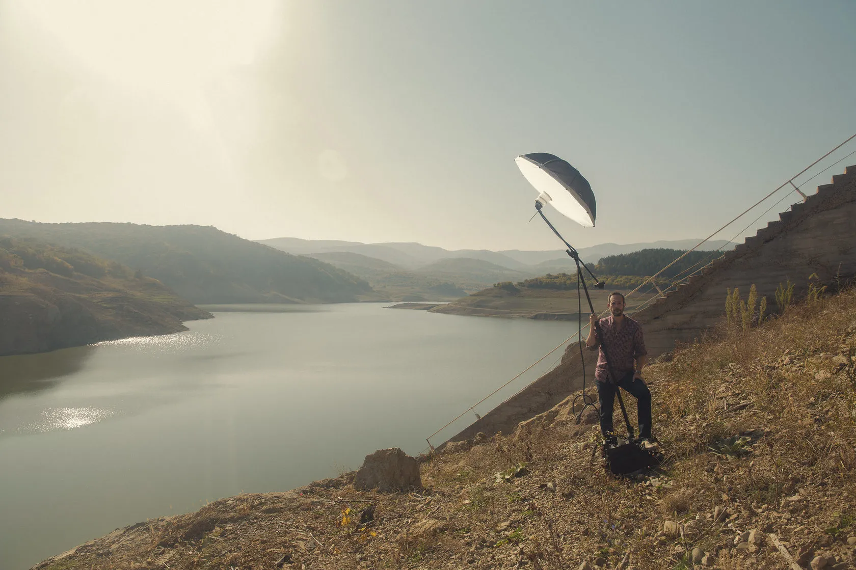 A crew member holds up a light on a pole on a dry hillside above a reservoir.