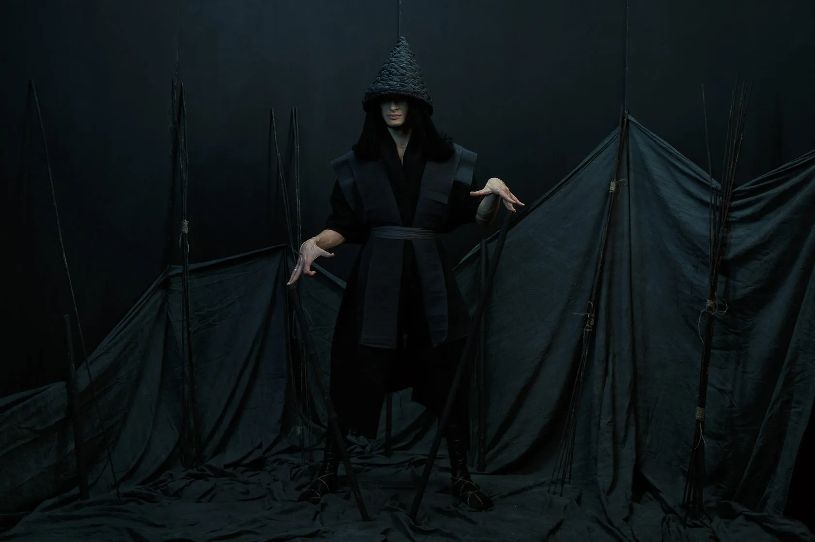 A Burito musician in a black costume and conical hat on a dark set of poles and cloth.