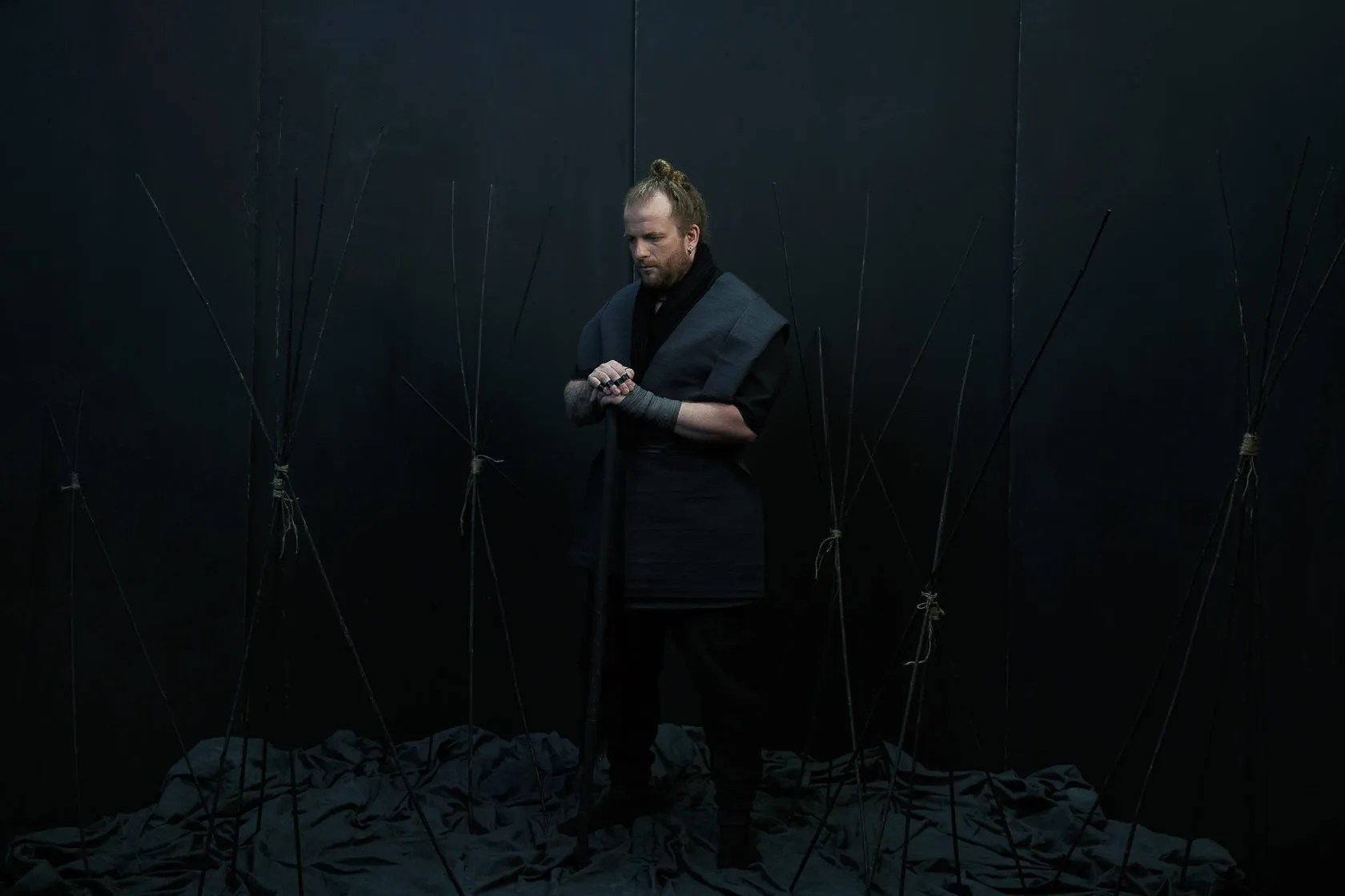 A Burito musician in a black samurai-style jacket fastens his cuff among black poles.