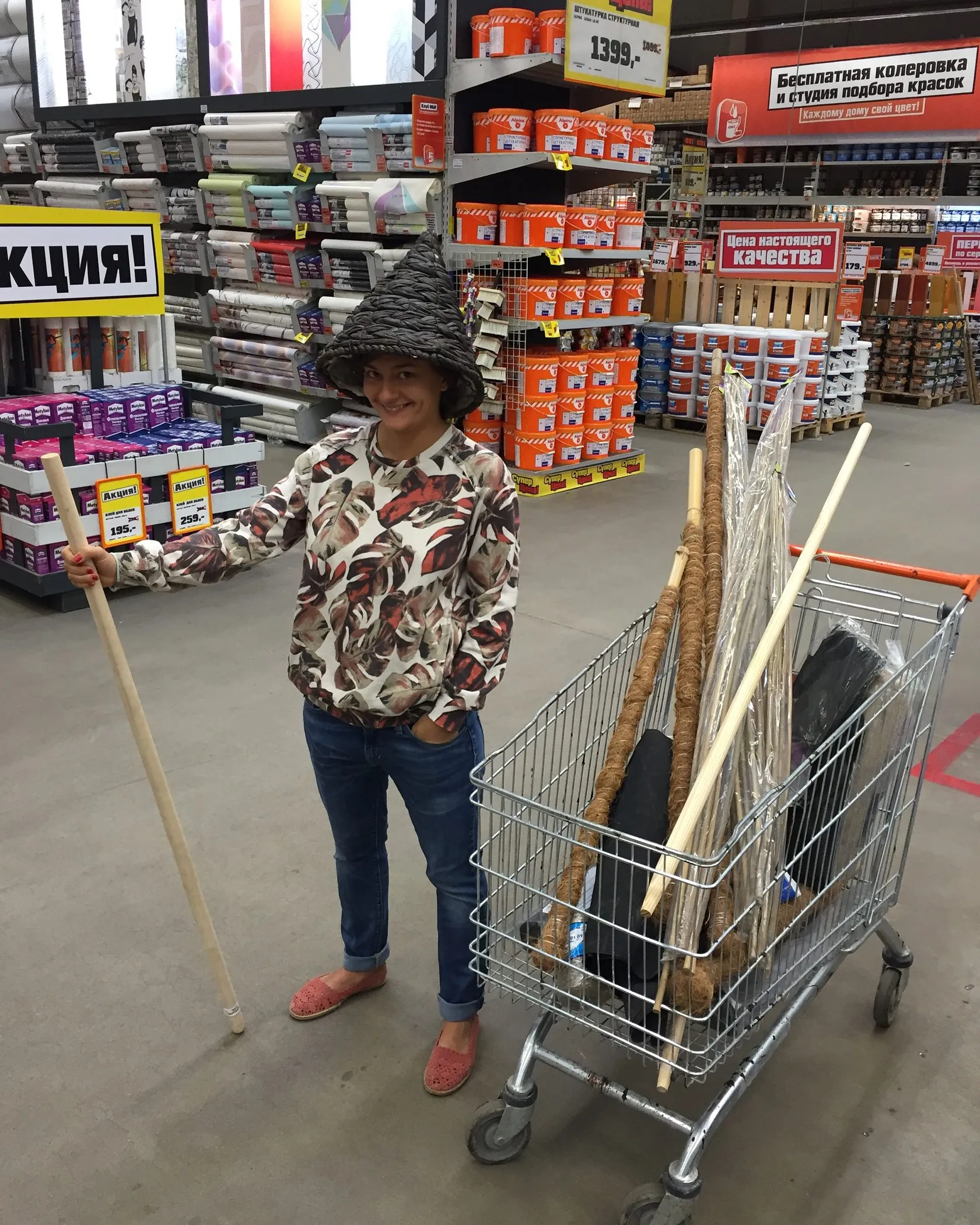 A woman in a woven hat with a trolley full of poles and boards in a DIY store.
