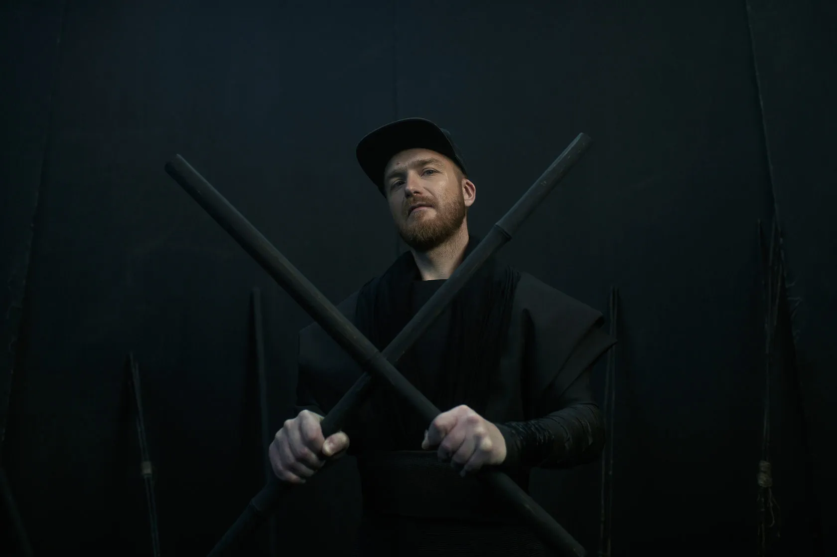 A man in a cap holds two black staffs crossed in front of him.