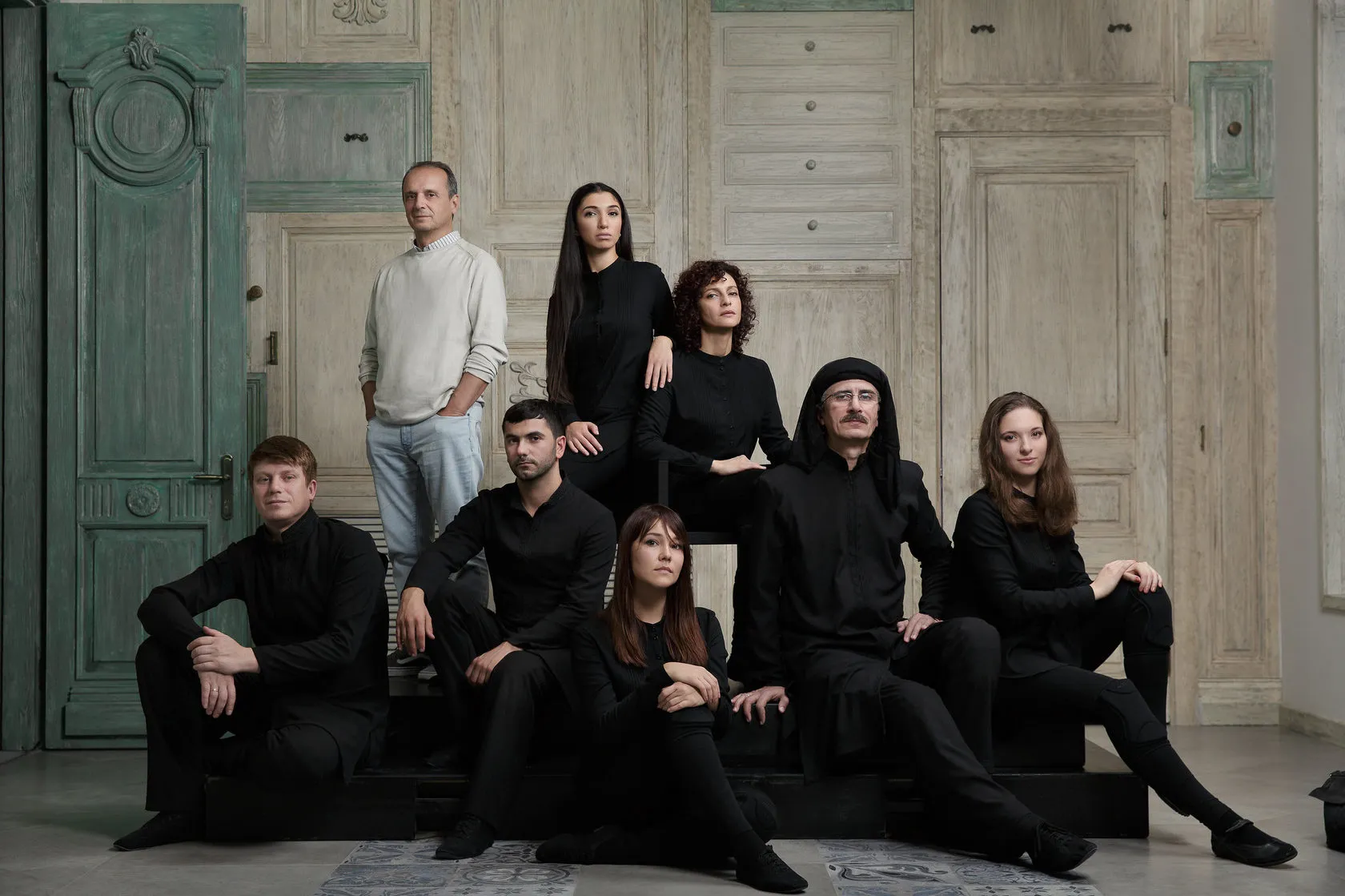 Tarlan Gorchu and his company, dressed in black, sit on steps before carved wooden panels.