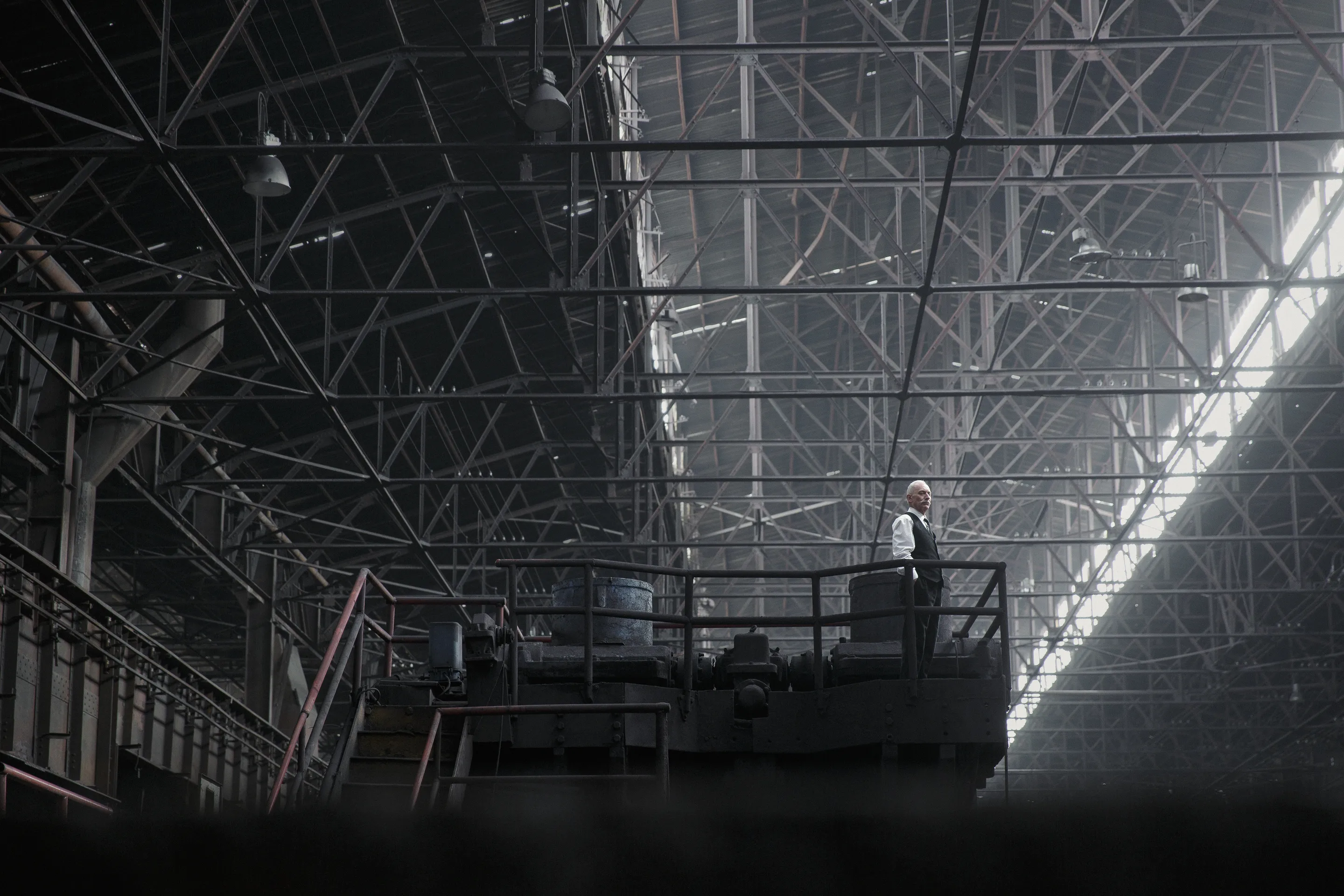 The Condemned of Altona key visual by Andrei Kovalev: a lone figure stands dwarfed beneath a vast steel roof truss.