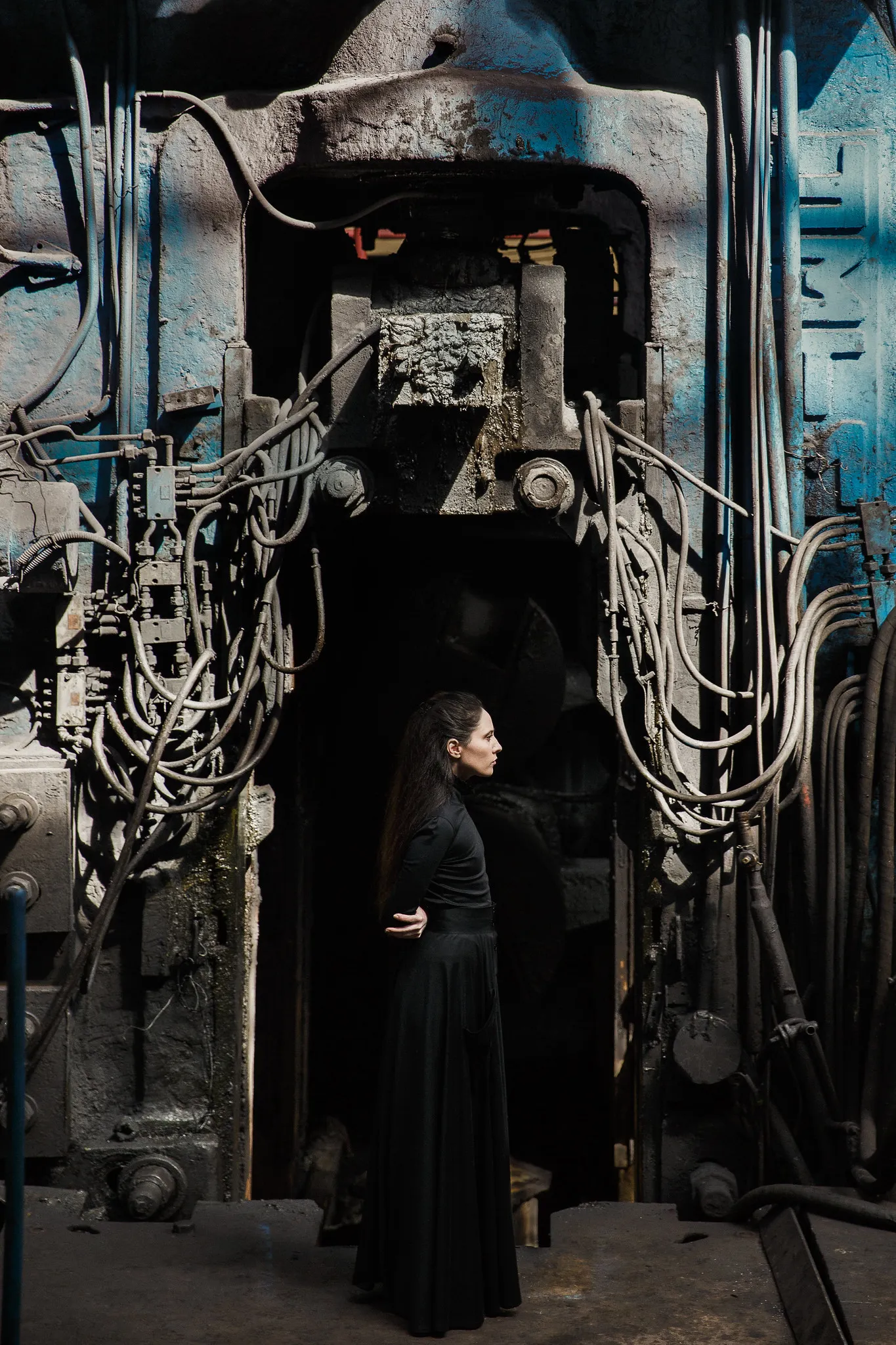 An actress in black stands beneath a huge machine hung with cables.