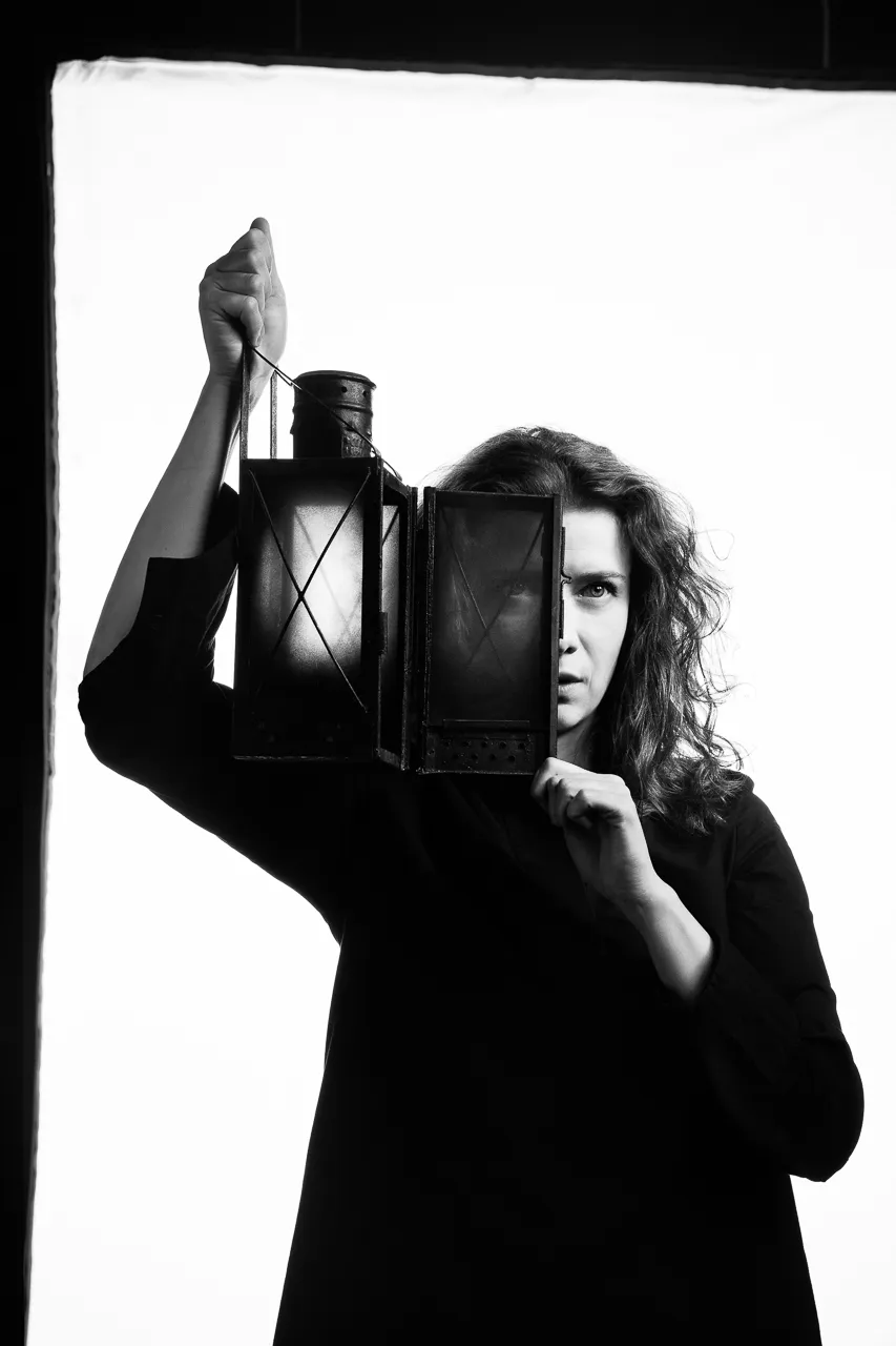 An actress raises an old lantern beside her face.